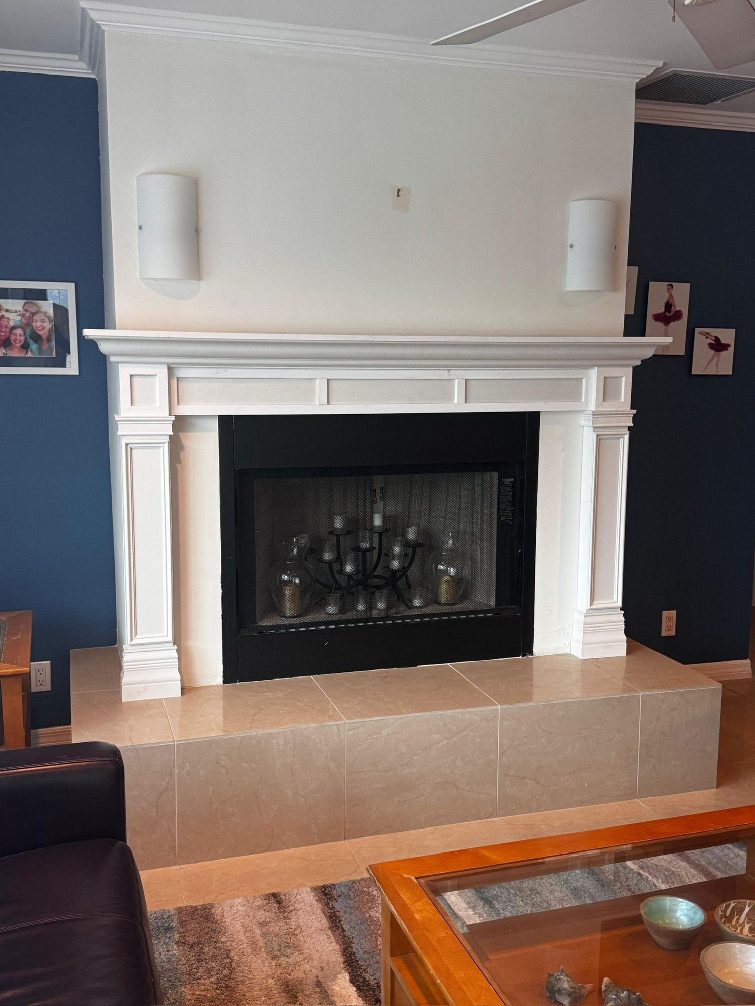 Empty living room fireplace with white mantel, black firebox, and blue walls, seen above a leather sofa and coffee table.