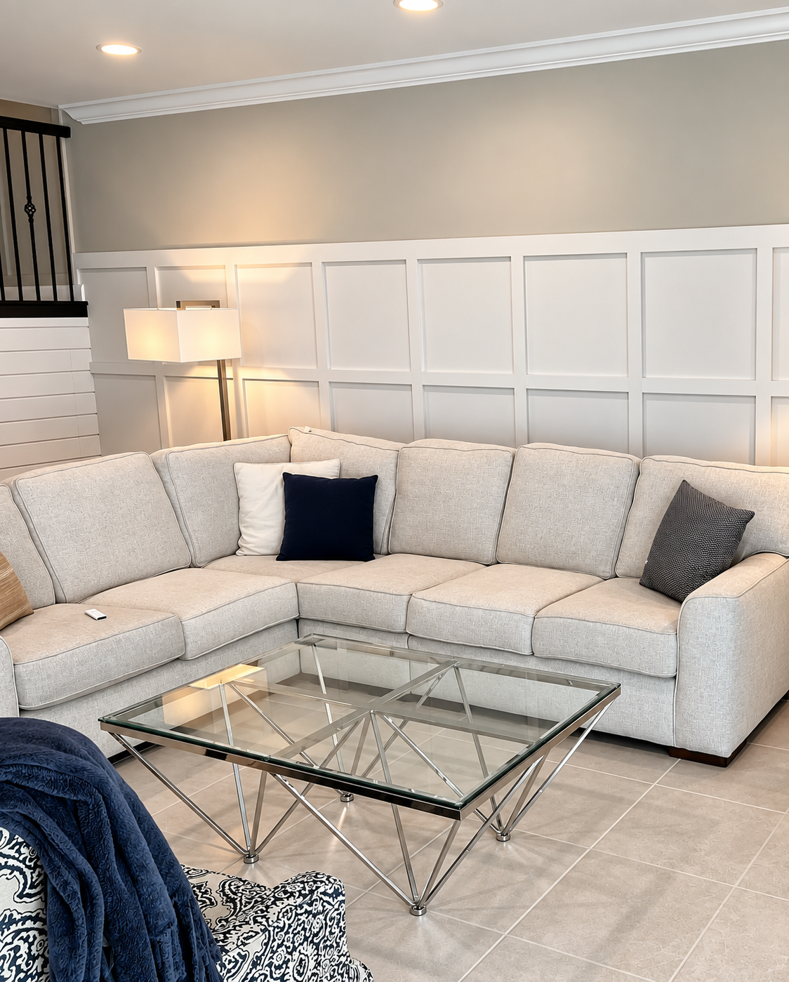 Bright living room with white sectional sofa, glass coffee table, floor lamp, and paneled wall trim