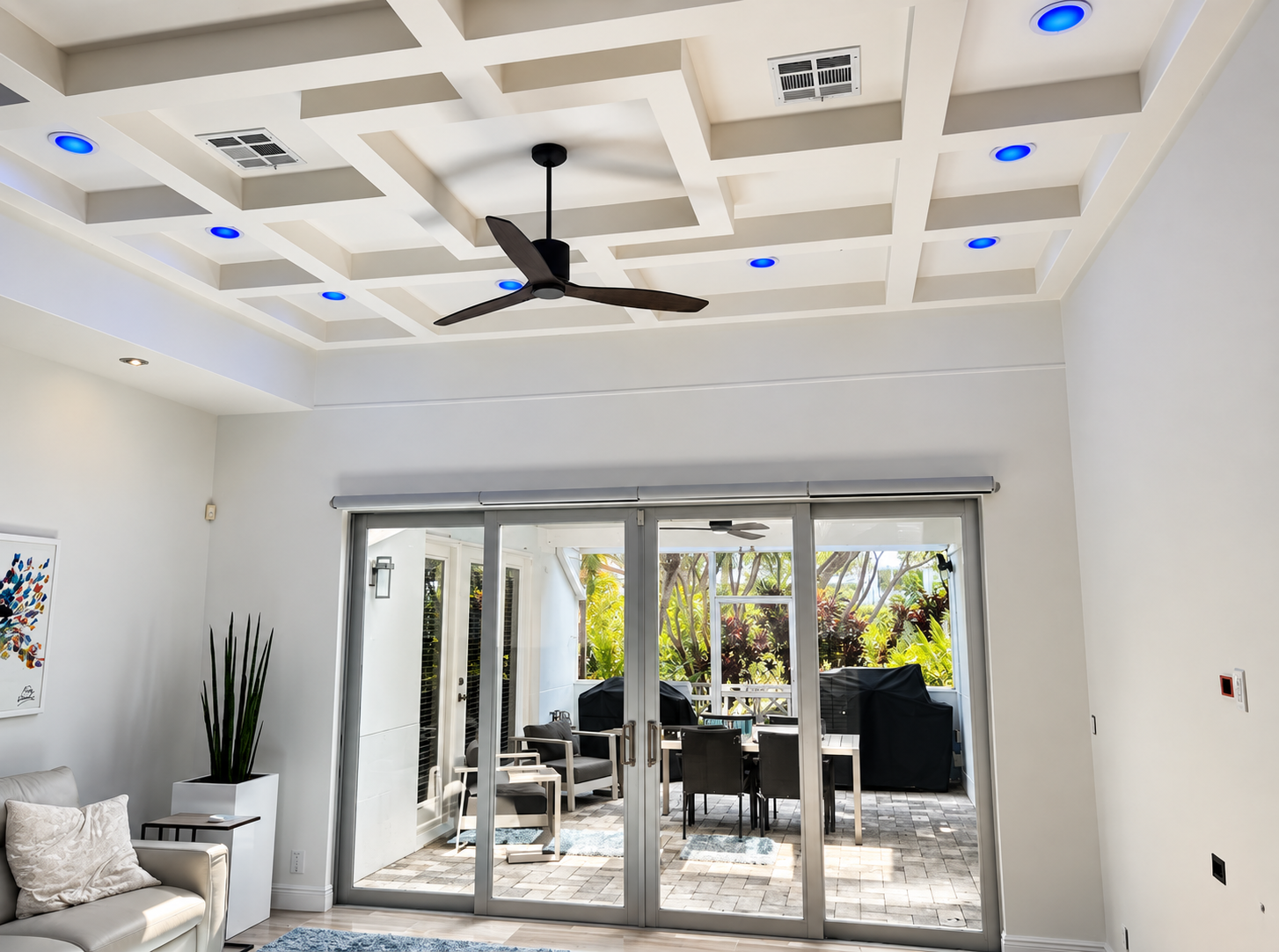 Bright living room with coffered white ceiling, black ceiling fan, and sliding glass doors to a patio.