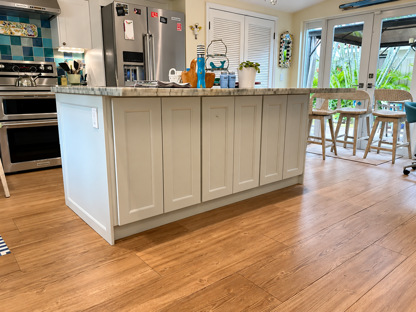 Bright kitchen with white island cabinets, stainless steel appliances, and a wood floor by a sunny window