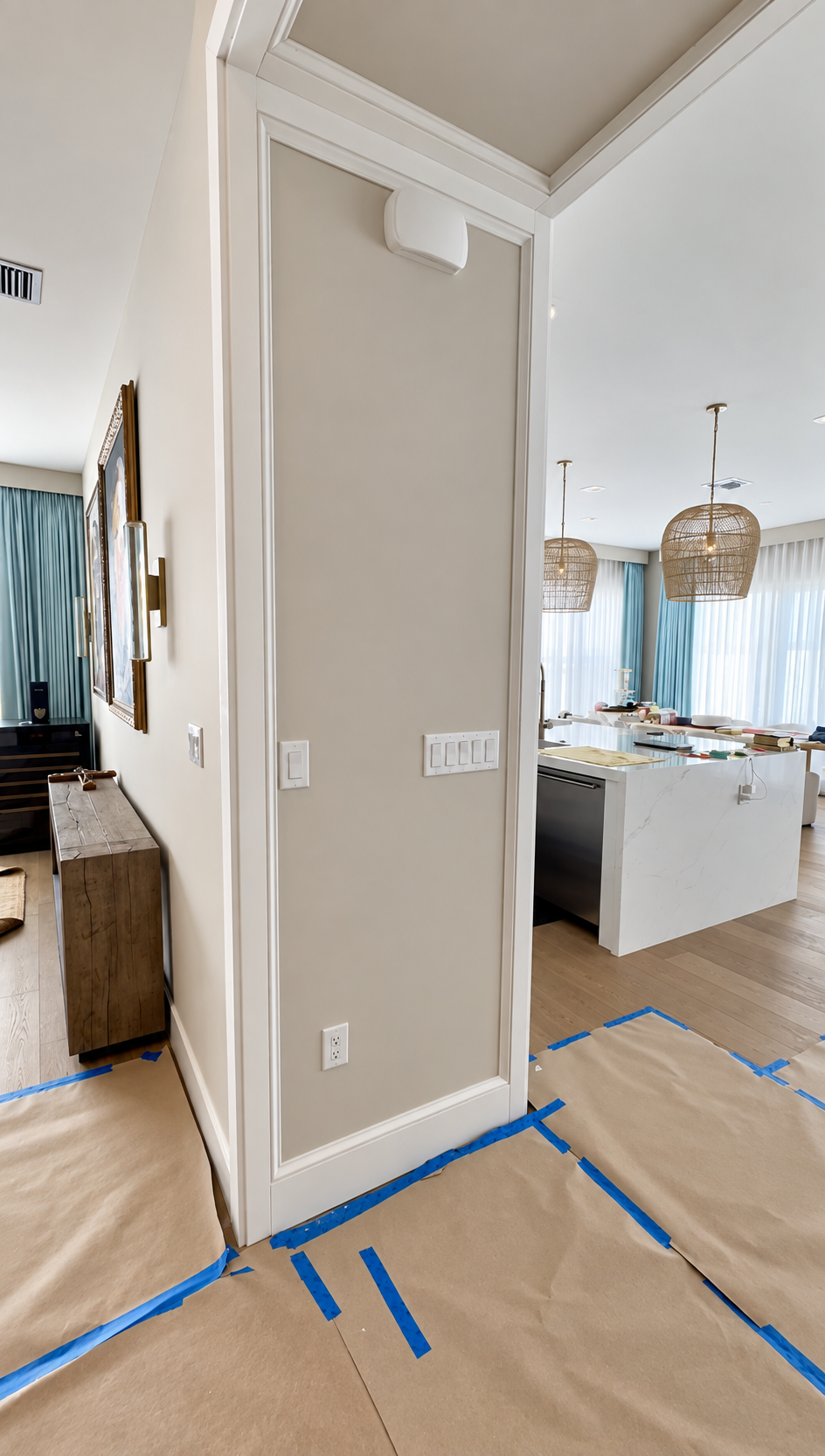 Interior hallway with beige walls, doorway trim, and blue painter’s tape on the floor near a kitchen.