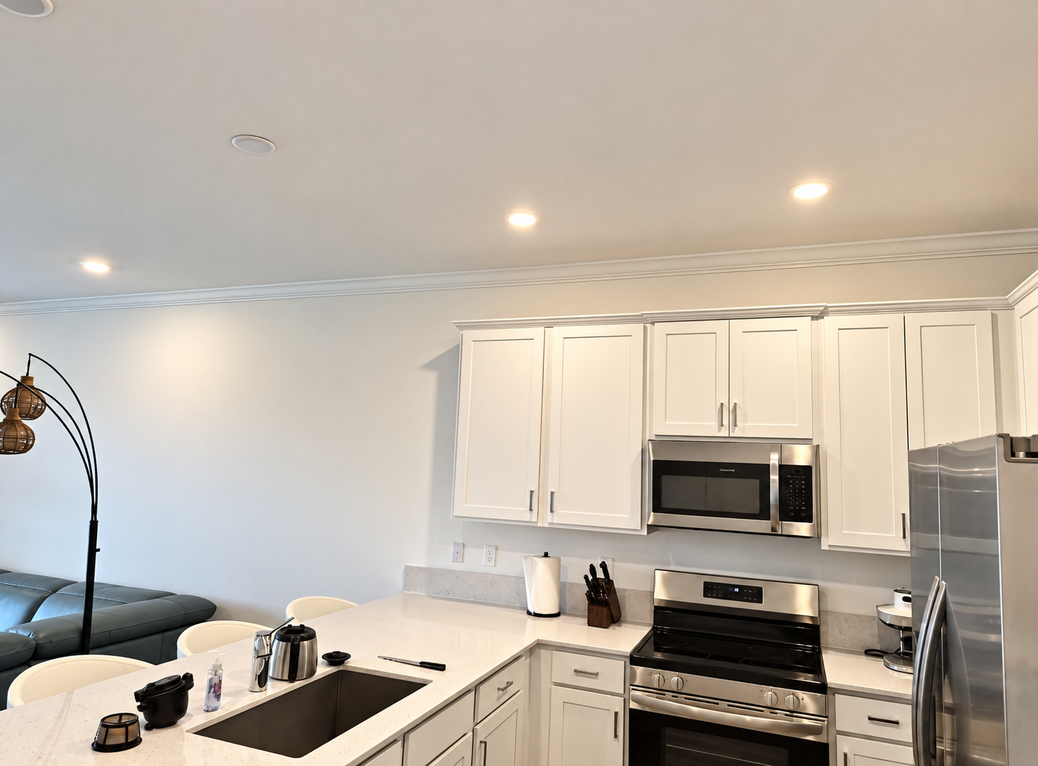 Bright modern kitchen with white cabinets, stainless appliances, and a living area in the background