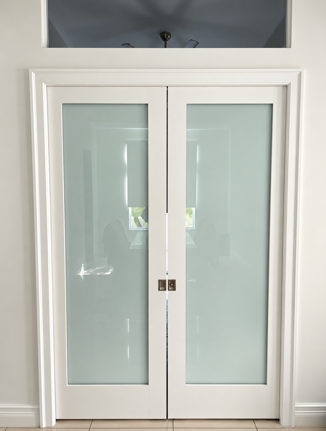 White double glass doors with frosted panels in a hallway, beneath a rectangular transom window.