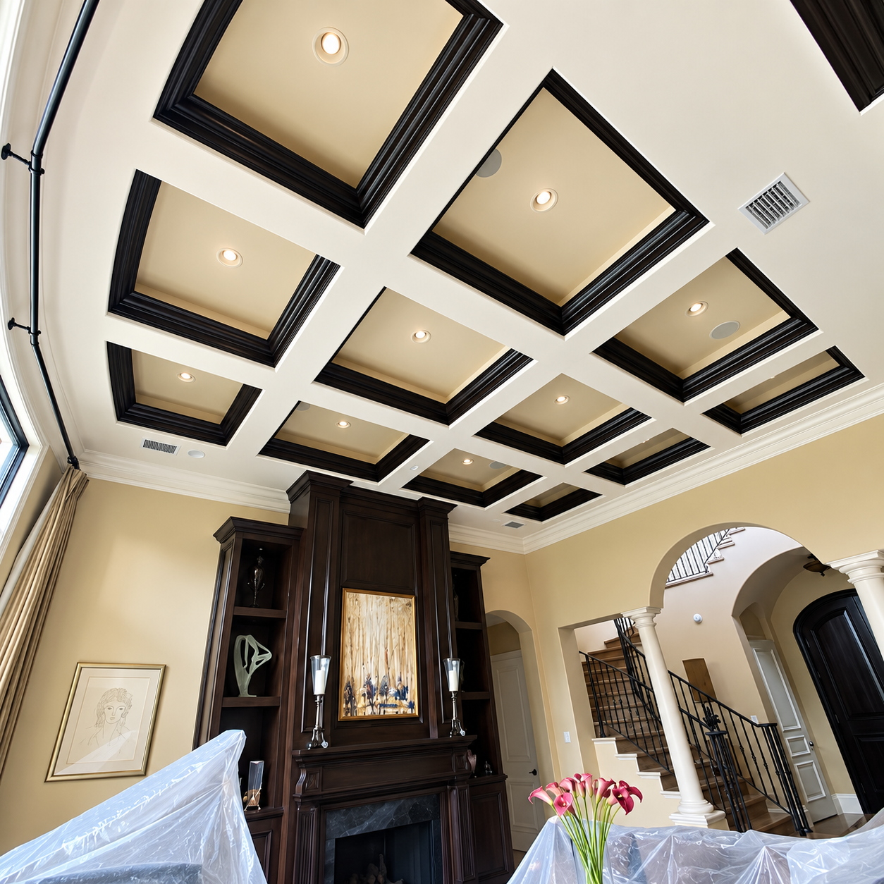 Elegant living room with coffered ceiling, recessed lights, dark wood cabinet, and staircase archway