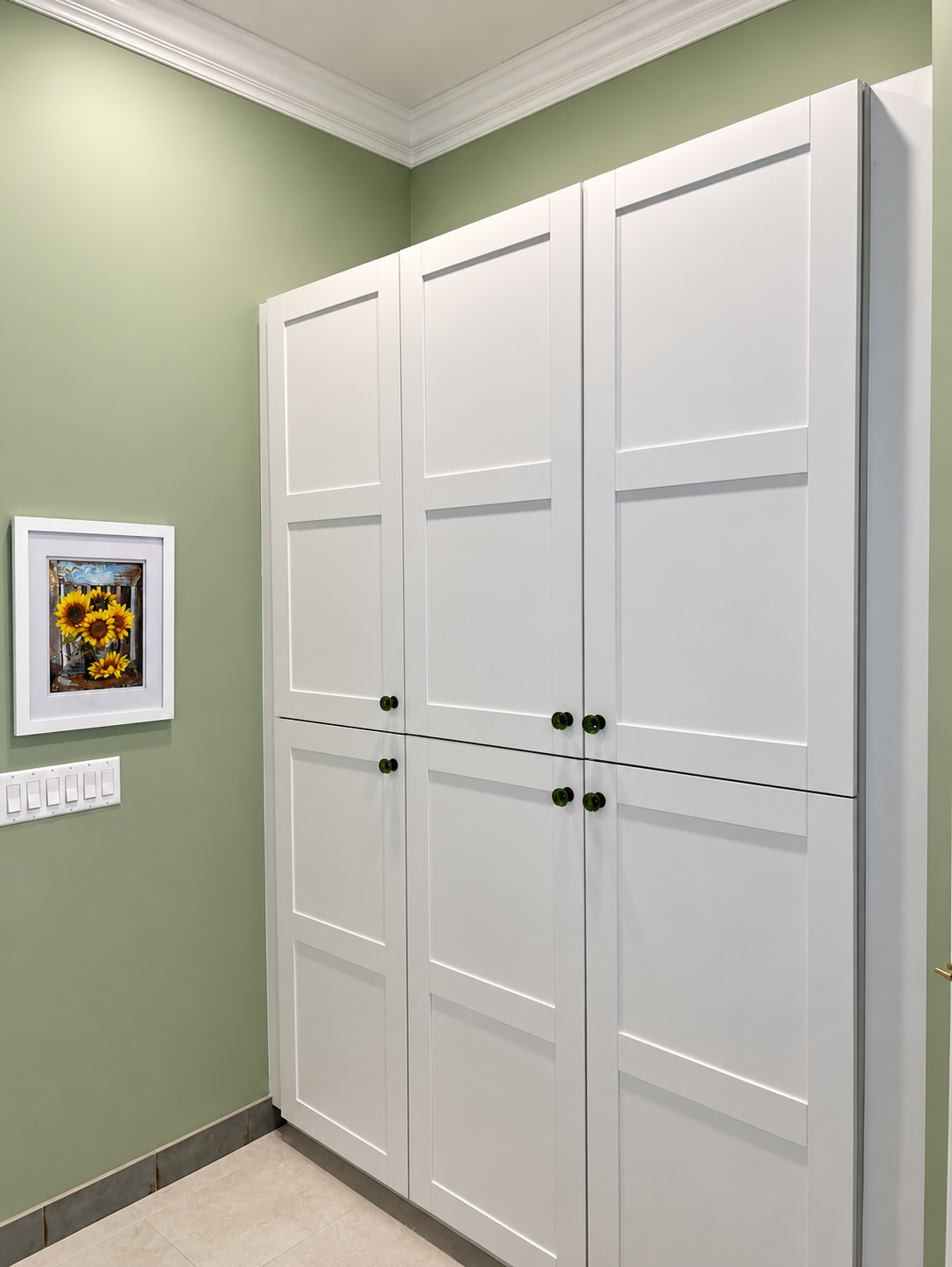 White paneled closet doors in a green room with crown molding and a small framed picture.