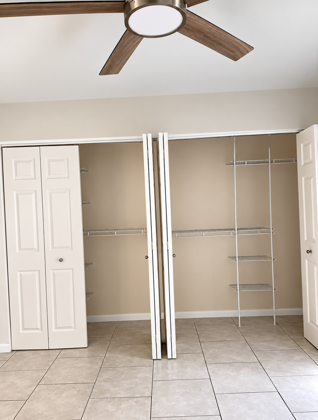 Empty bedroom closet with open white doors, wire shelving, beige walls, and tiled floor