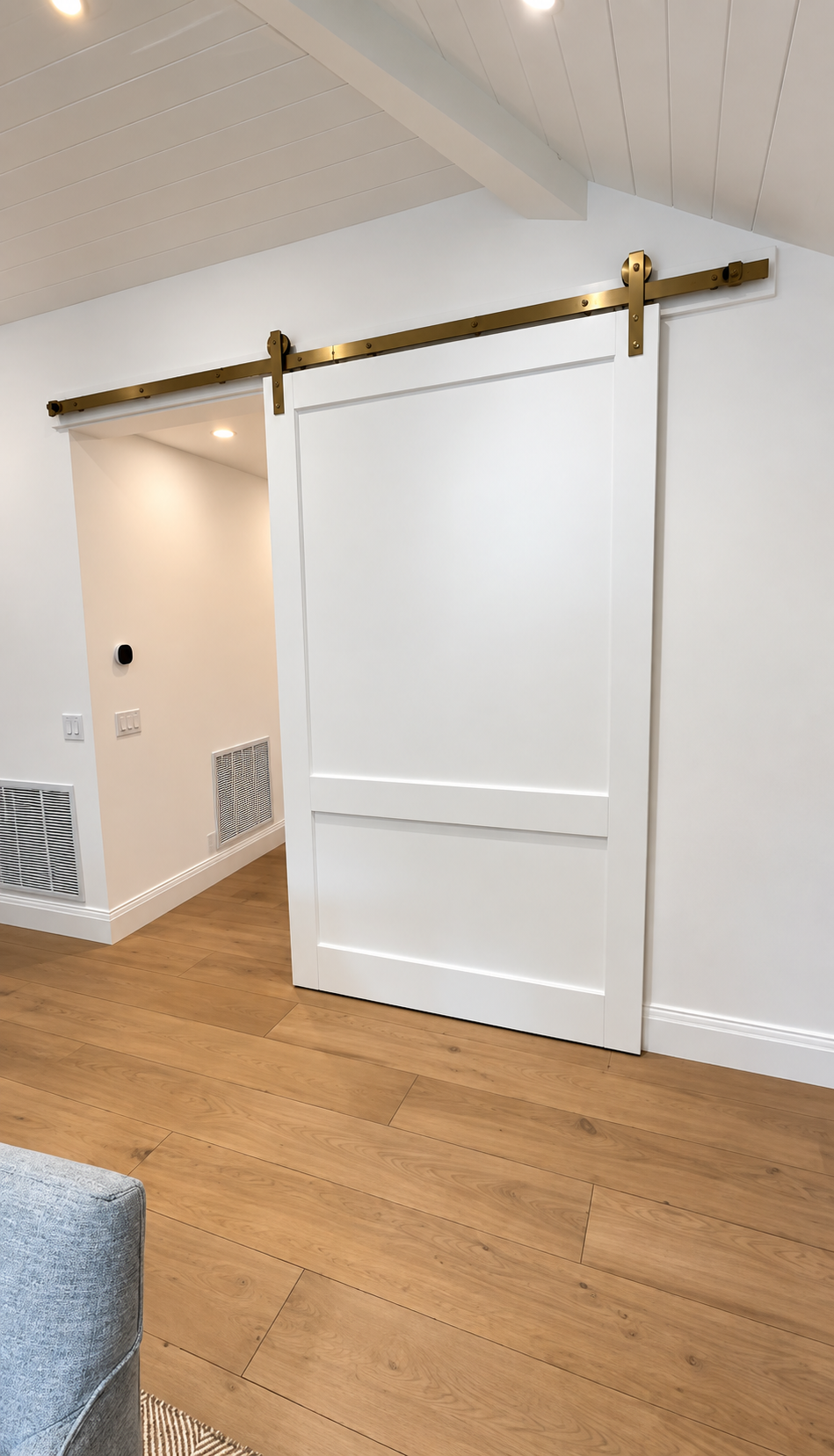 White barn-style sliding door with brass track in a room with wood floor and beige walls.