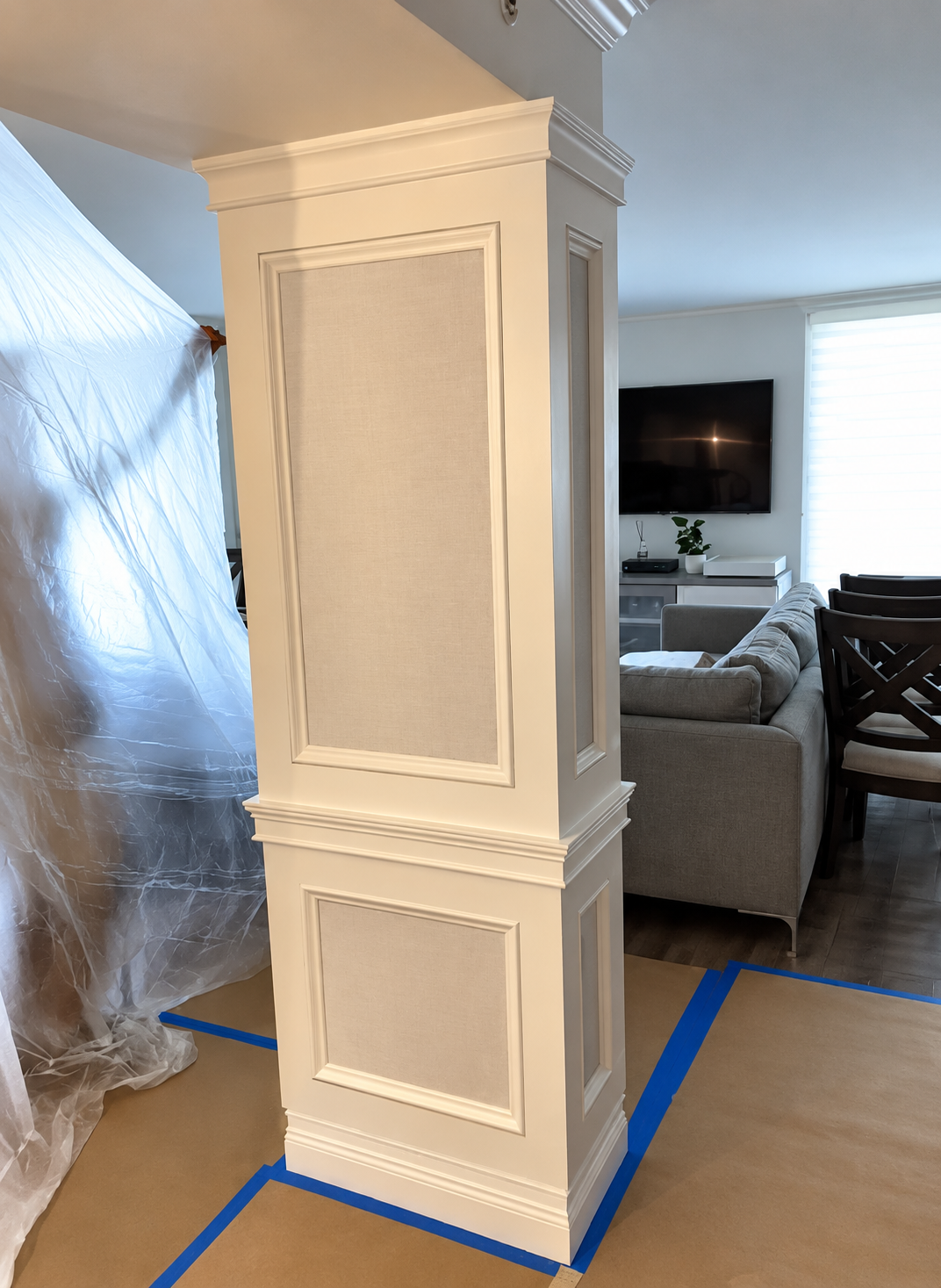 Cream-painted decorative column in a living room, surrounded by blue painter’s tape and plastic sheeting.