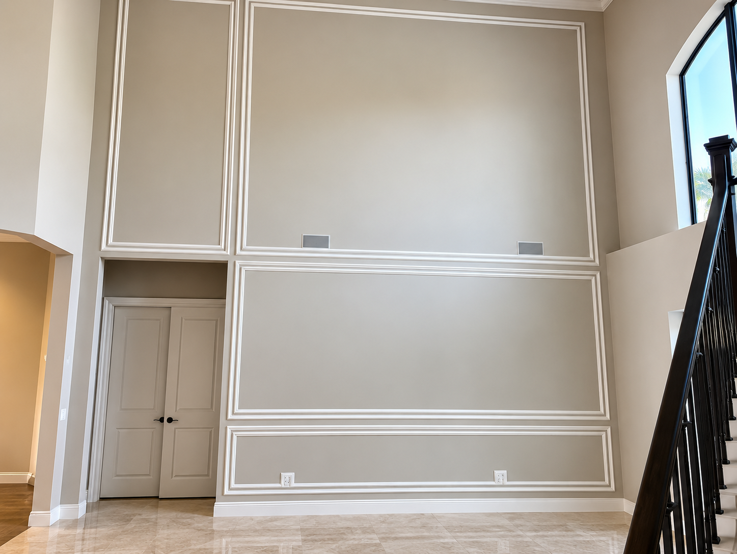 Empty beige living room with tall walls, decorative molding, and a staircase on the right