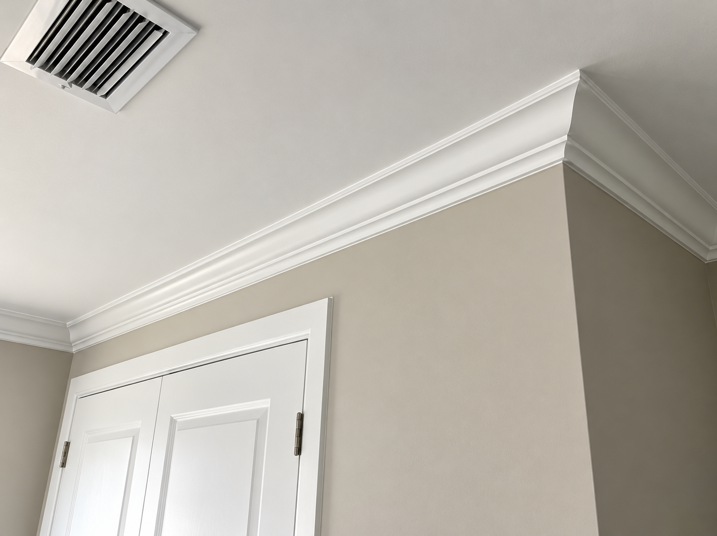 White crown molding on a beige room corner with a ceiling vent and white closet doors
