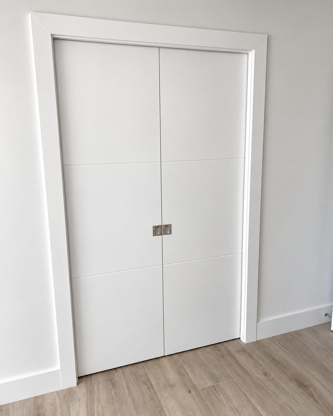 White double closet doors with a small latch in a plain room with light wood flooring.