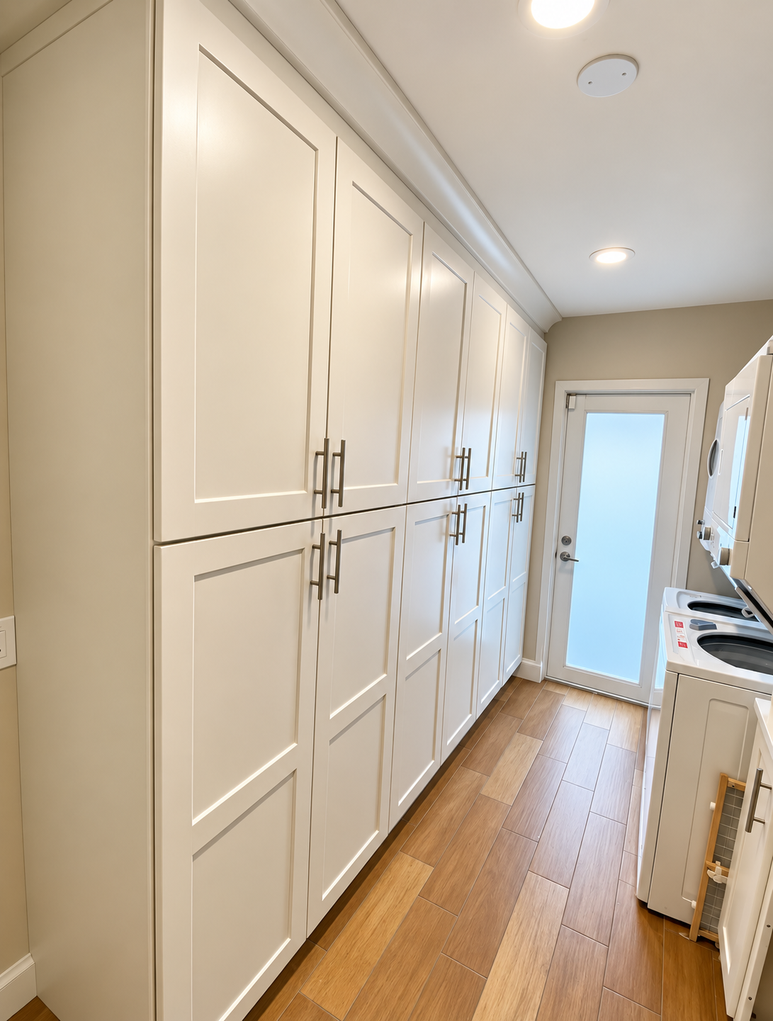 Narrow white laundry room with built-in cabinets, wood floor, and a door at the end.