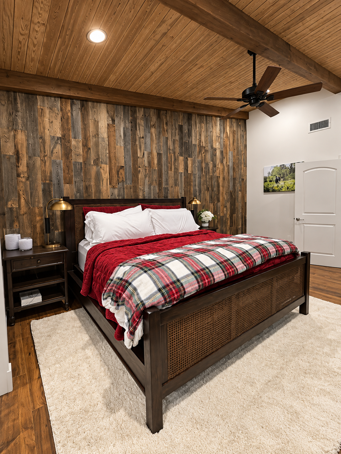 Cozy rustic bedroom with wood-paneled walls, a red plaid bedspread, ceiling fan, and white refrigerator.
