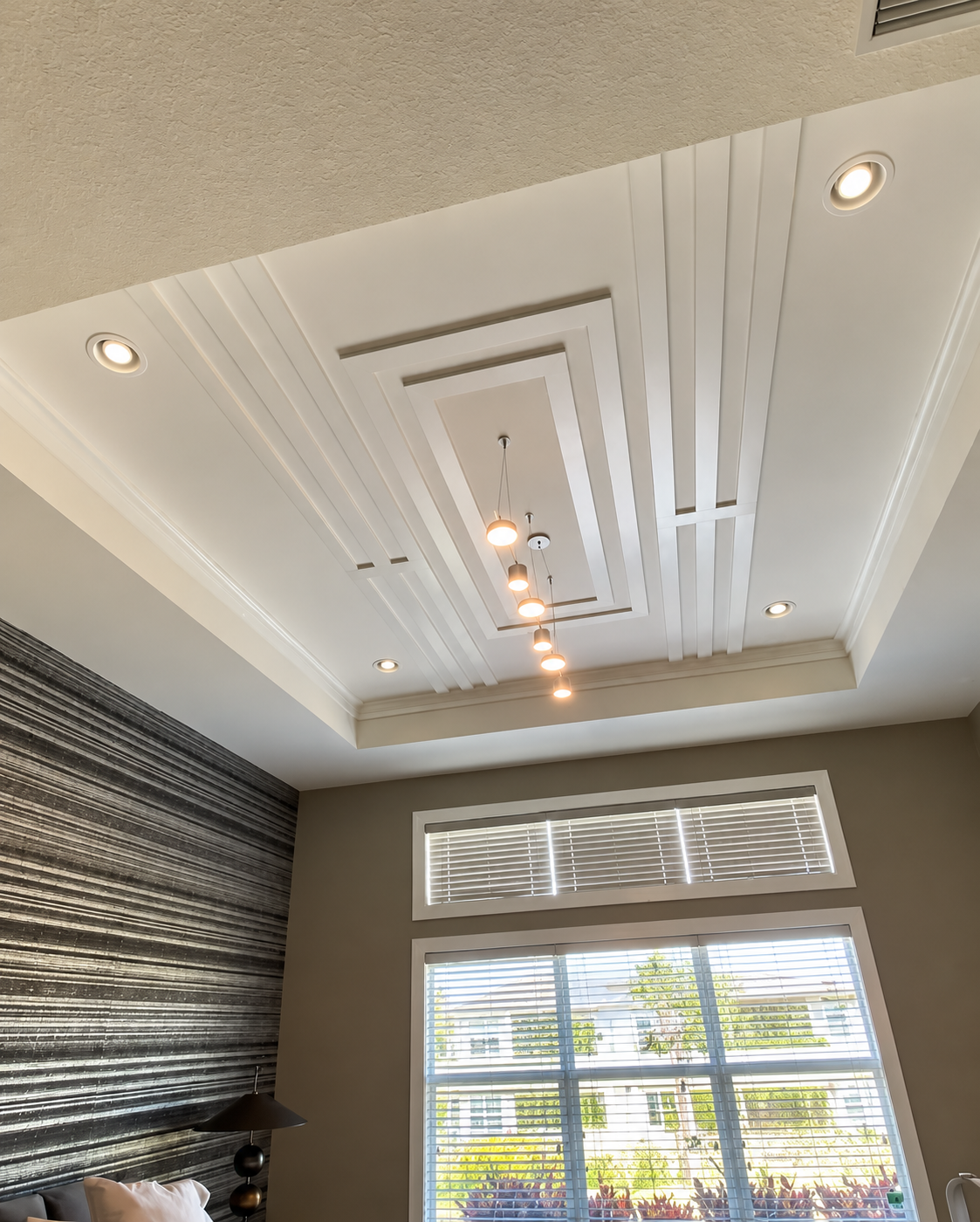 White tray ceiling with recessed lights above a window with blinds in a modern room