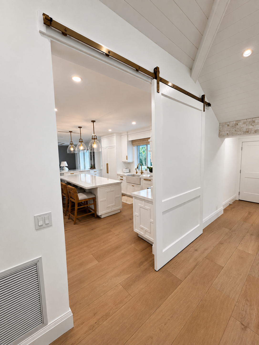 Bright kitchen with white cabinets, wood floors, and a large barn door opening to another room
