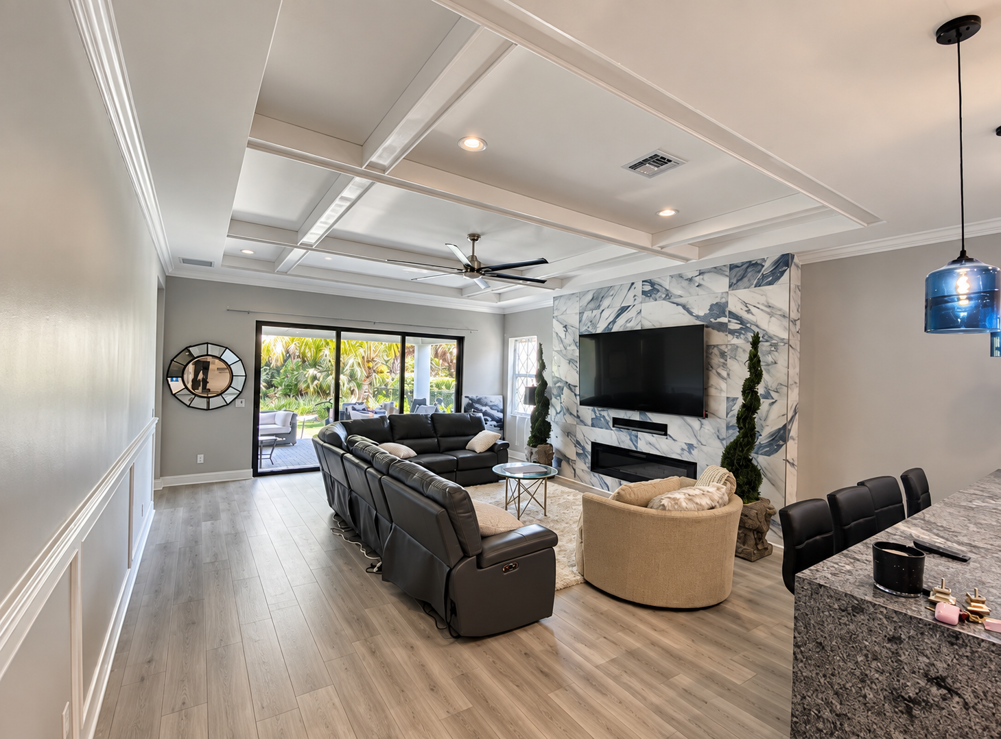 Bright modern living room with black sectional, wall TV, marble accent wall, and large windows.