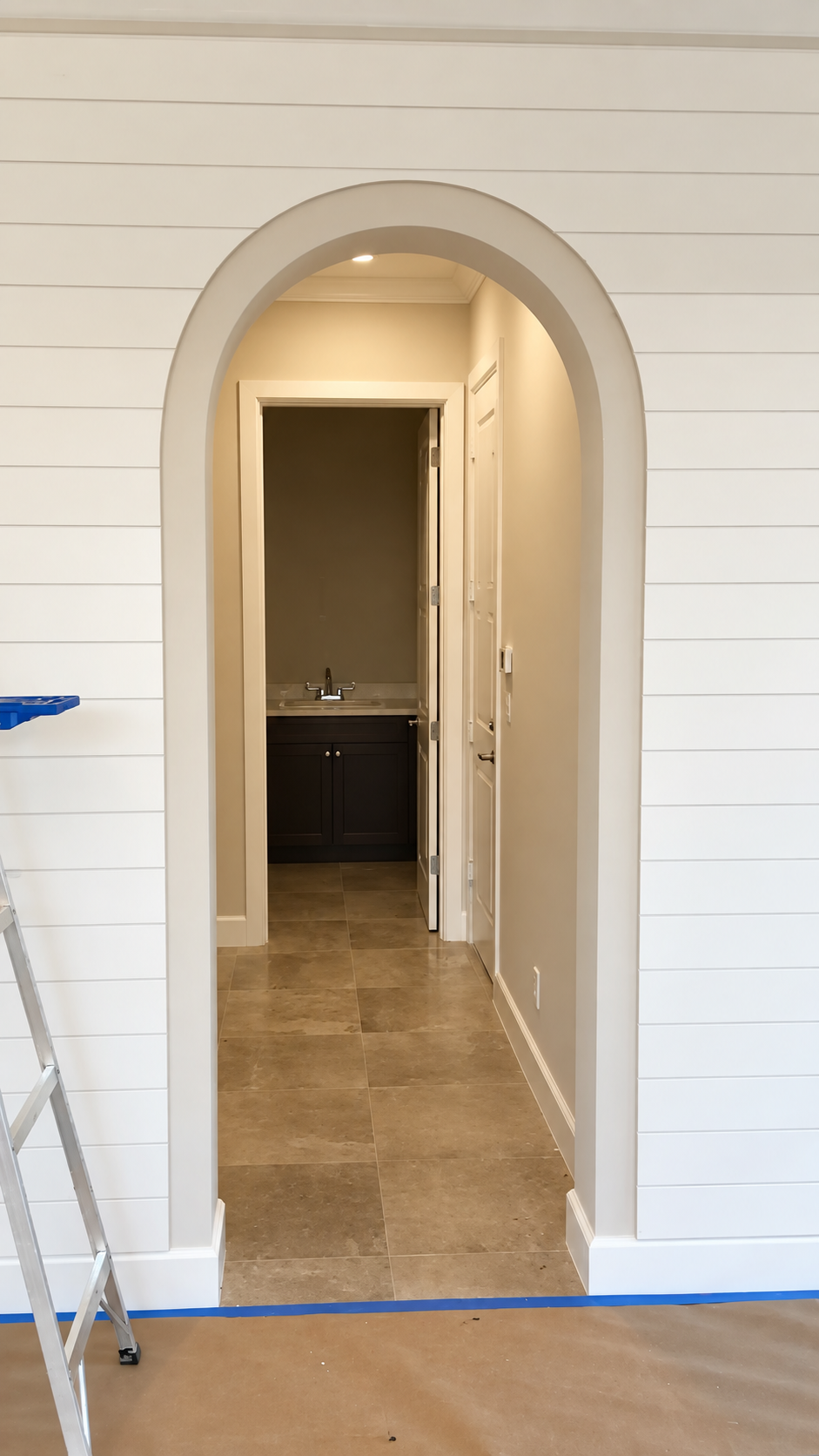 Arched doorway leading to a beige hallway with a dark cabinet at the far end and a blue-taped floor edge