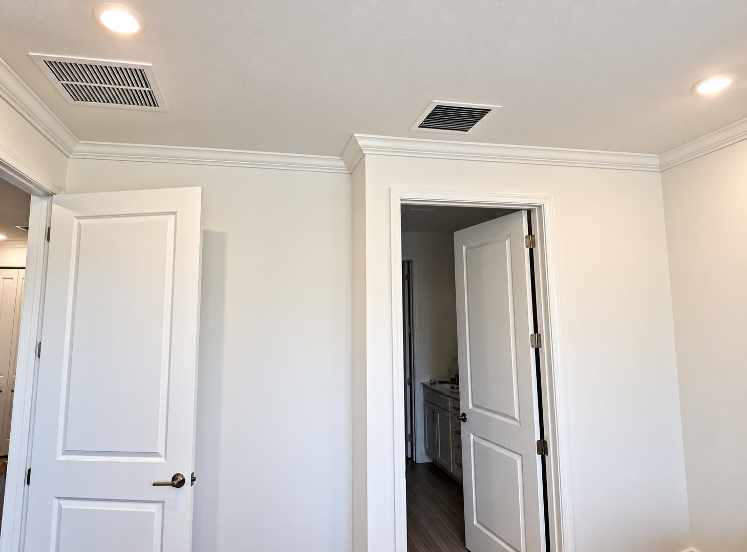 White bedroom with two open doors, recessed lights, and ceiling vents on a light-colored wall