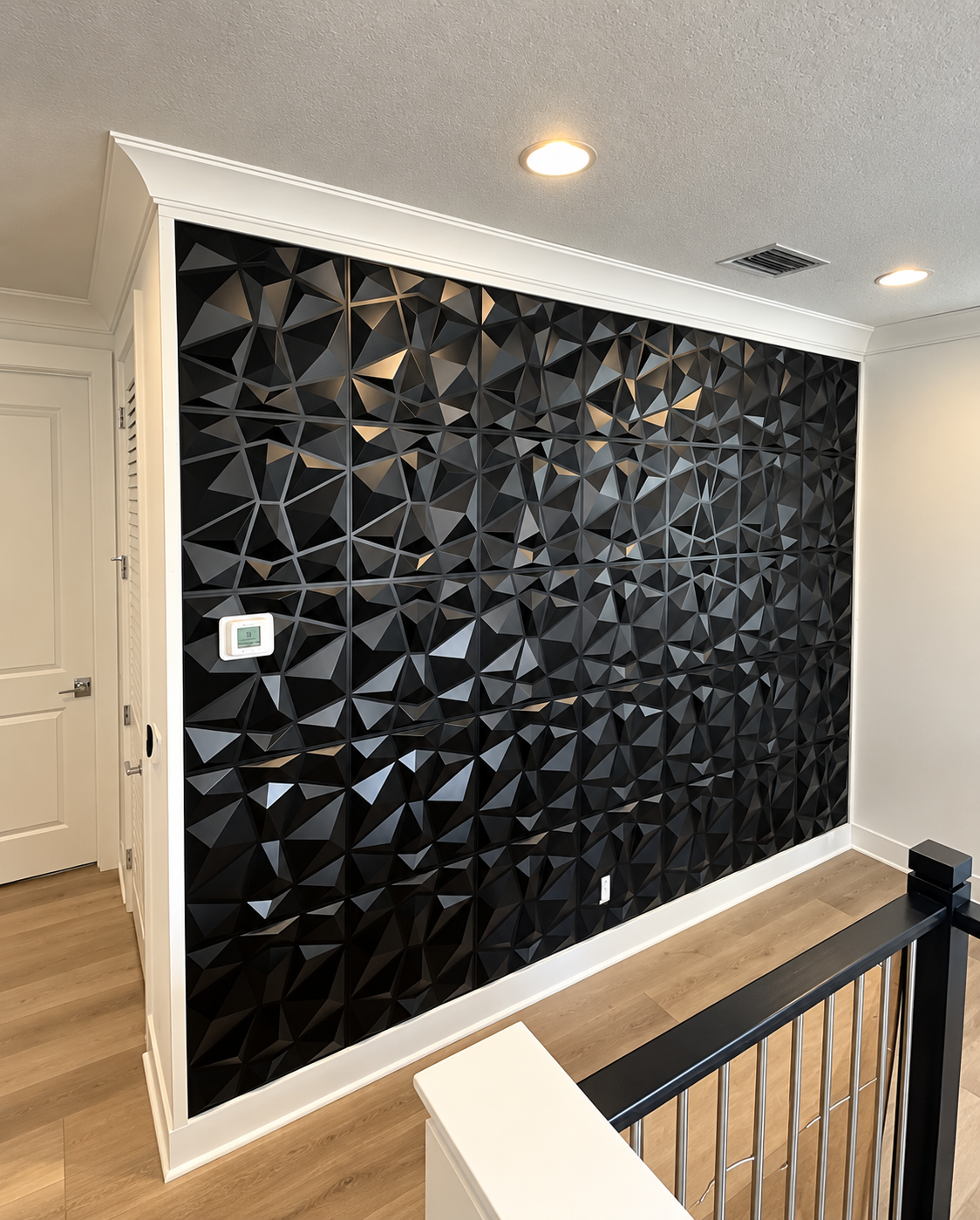 Black 3D geometric accent wall in a white hallway with recessed ceiling lights and railing in foreground