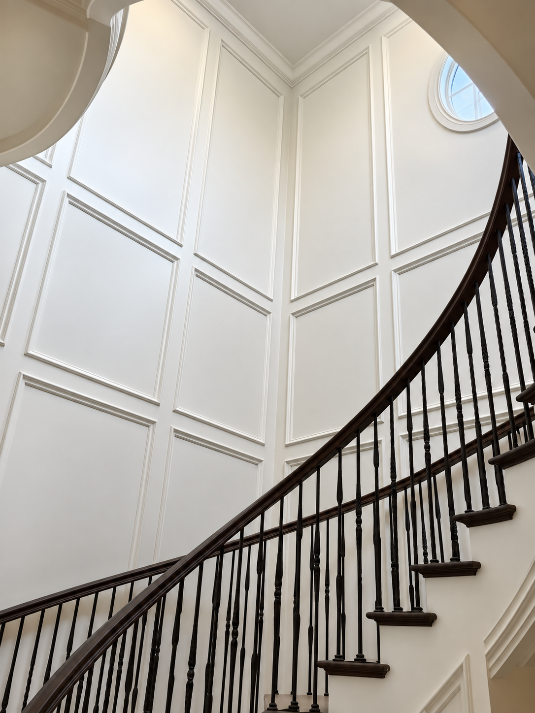 Curved staircase with dark railing in a bright white paneled foyer