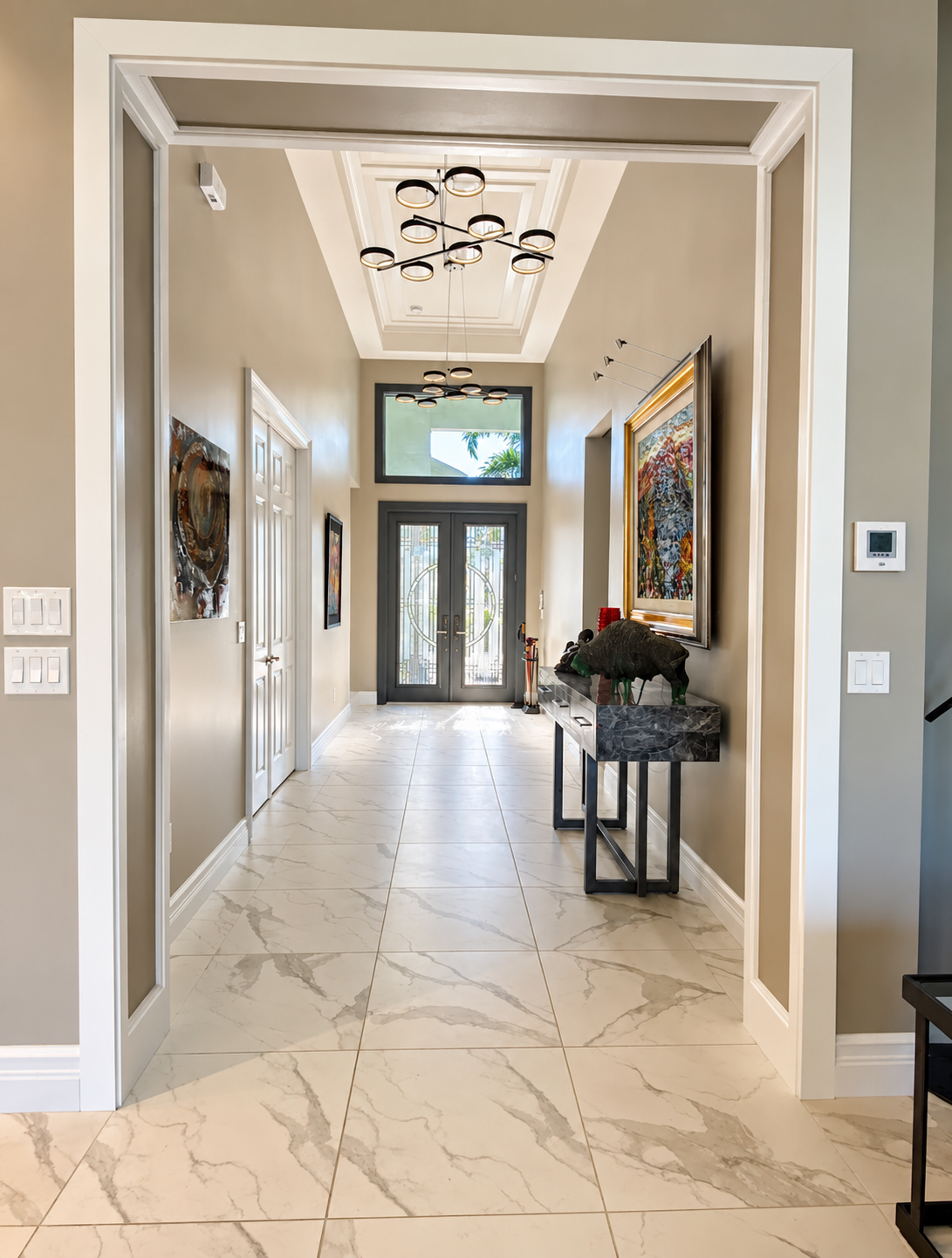 Bright marble foyer with a chandelier, console table, wall art, and glass front doors.