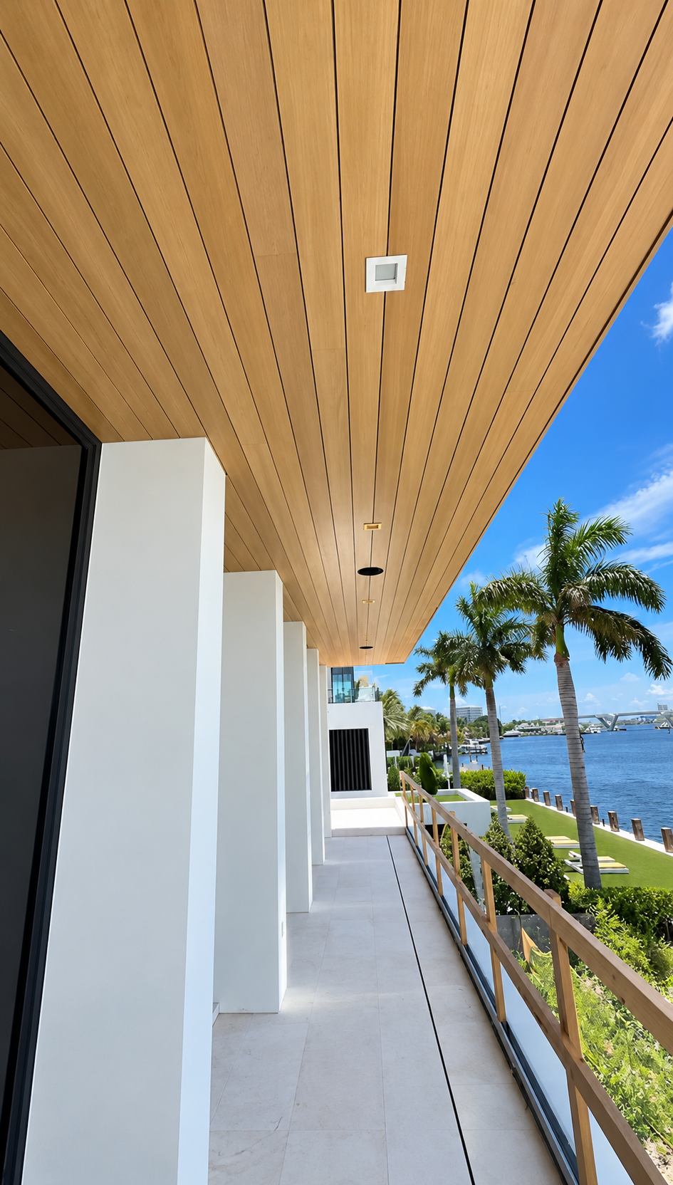 Modern seaside walkway with wood ceiling, white columns, palm trees, and ocean view