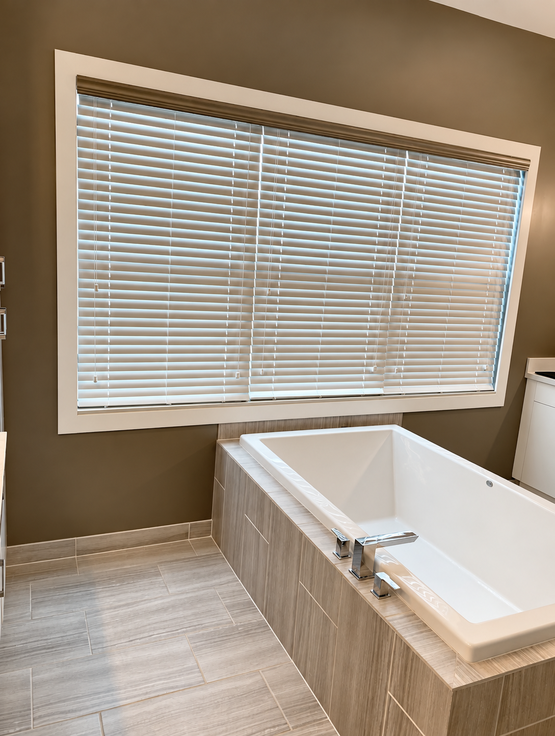 Modern bathroom with a white soaking tub, window blinds, and tan walls