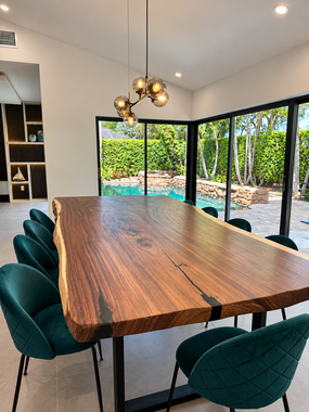 Modern dining room with a long wooden table, green chairs, and floor-to-ceiling windows overlooking a garden.