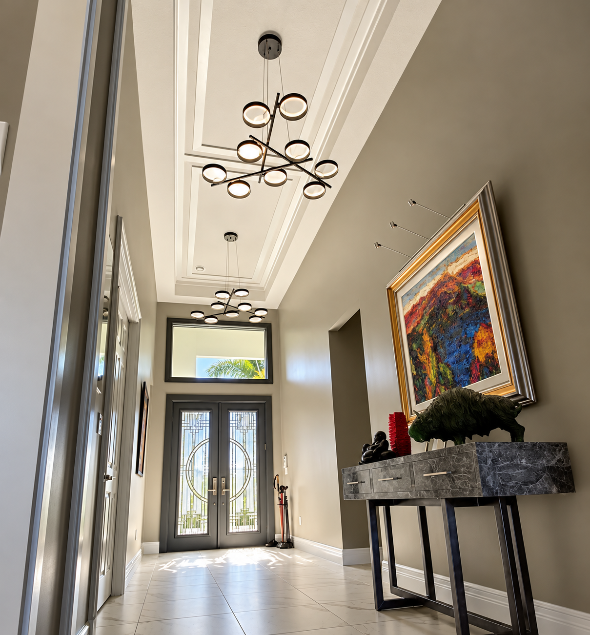 Modern entryway with high ceiling, pendant lights, double doors, and a console table with colorful art.