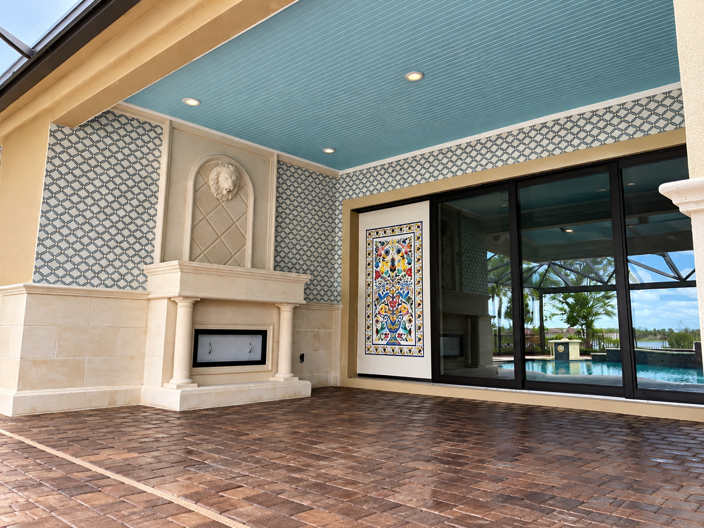 Covered patio with fireplace, patterned blue ceiling, tiled floor, and sliding glass doors overlooking a pool.