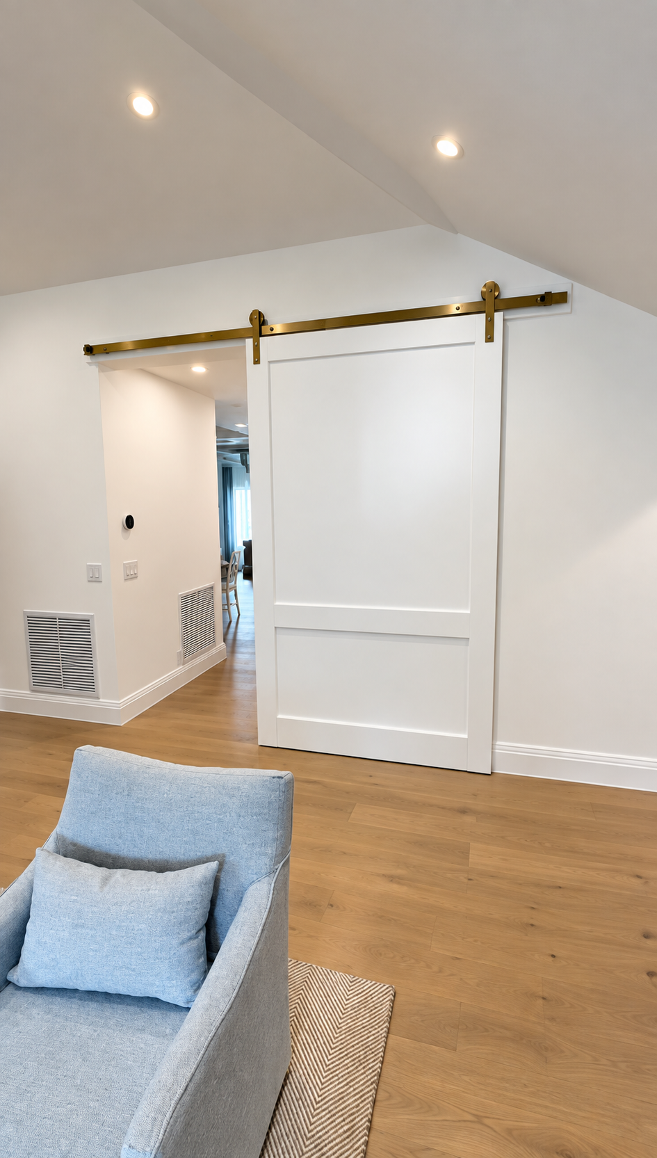 Bright living room with white barn door, light wood floor, and a blue sofa in the foreground