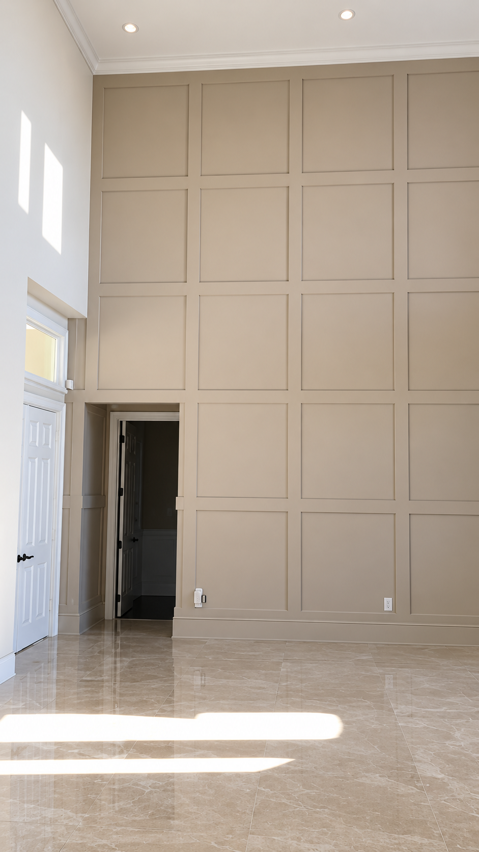 Tall beige paneled wall in a bright empty room with tiled floor and sunlight from side windows
