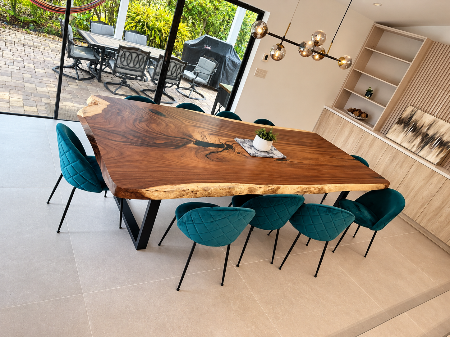 Modern dining room with a live-edge wooden table, teal chairs, and a view of the patio.