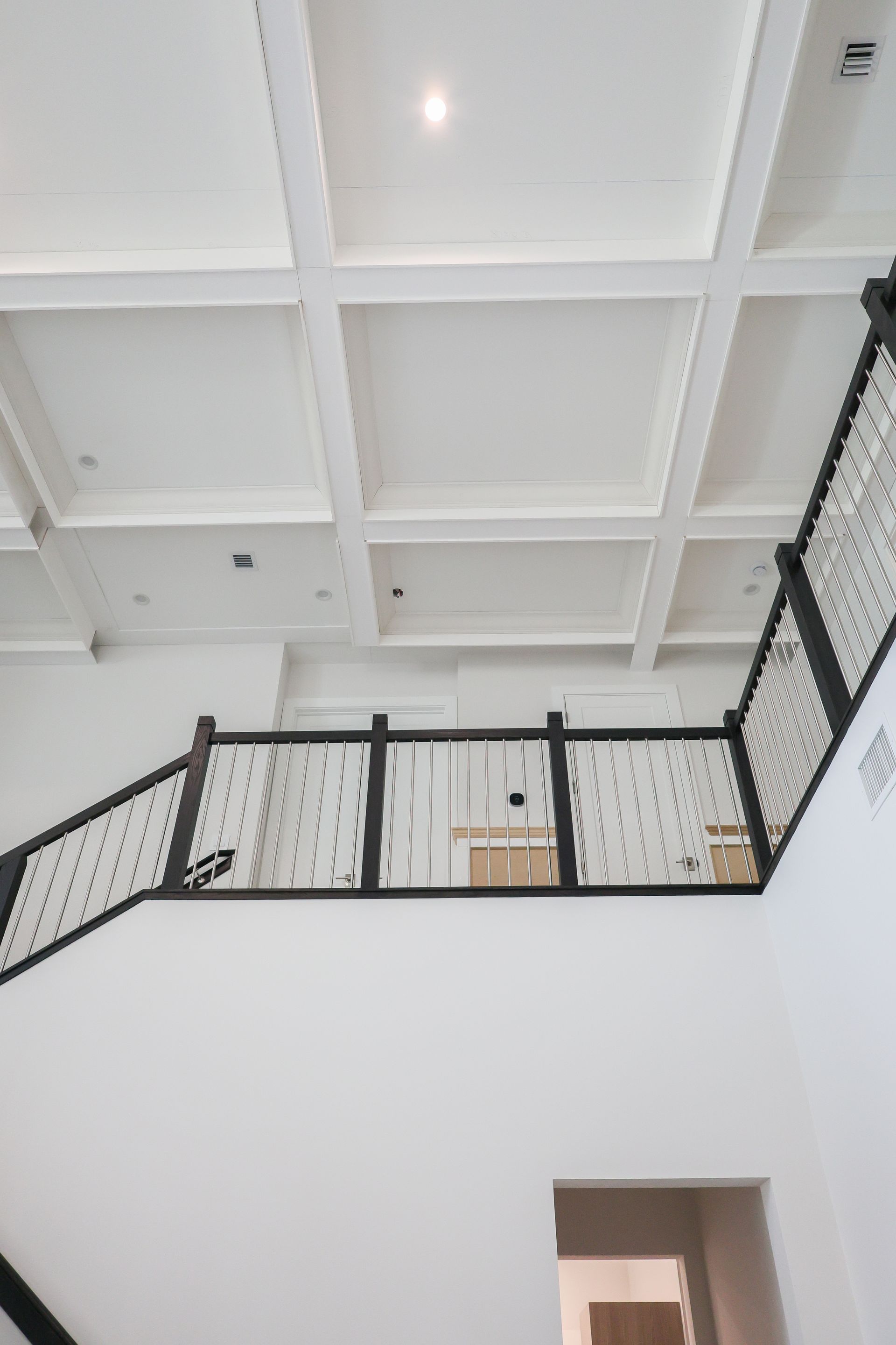 White interior with a black mesh balcony railing and coffered ceiling overhead