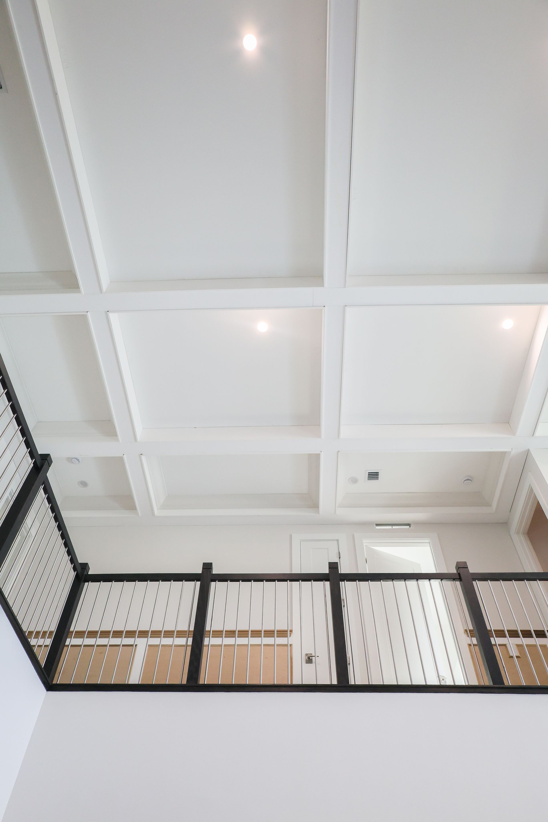 White coffered ceiling above a black metal railing in a bright indoor atrium