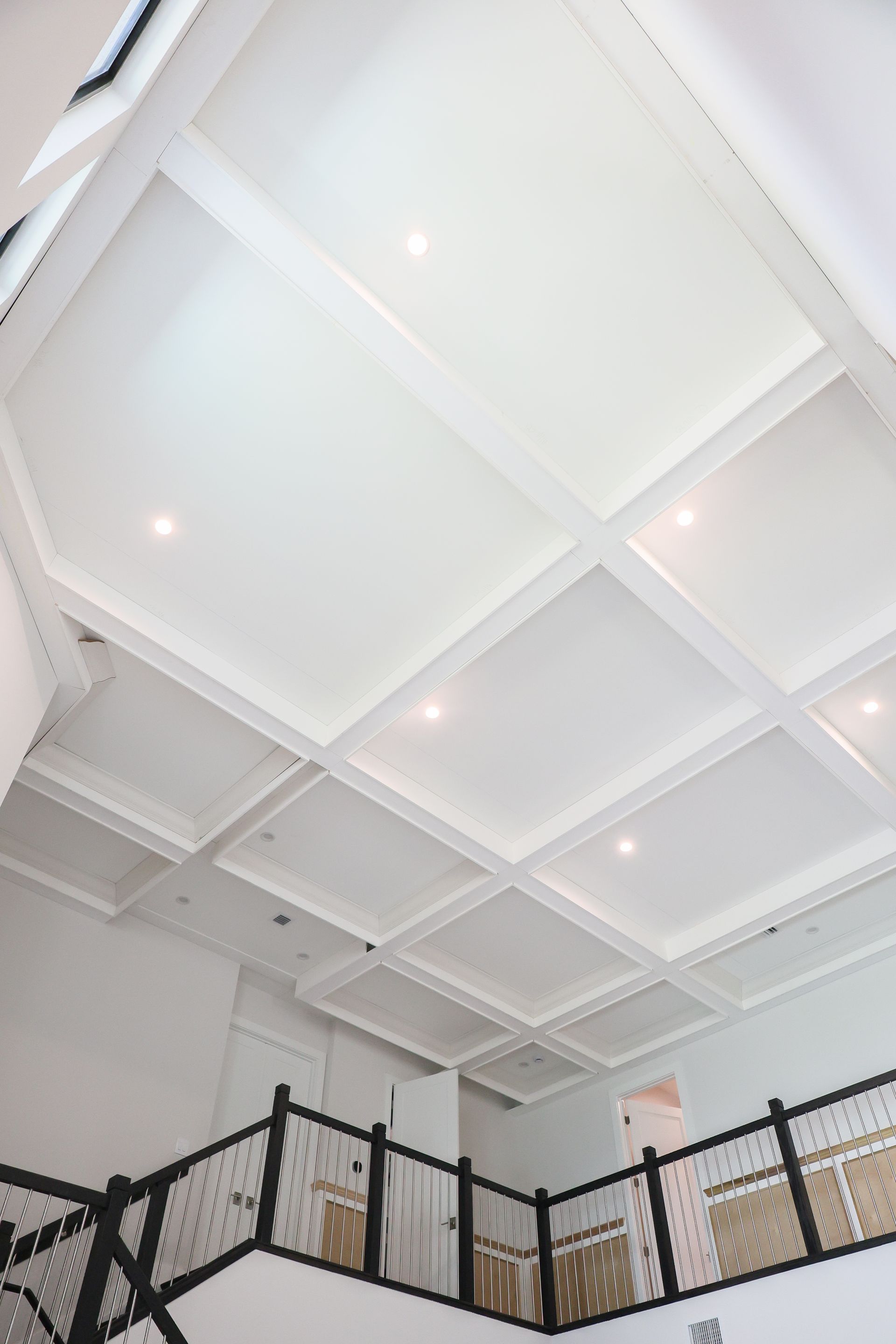 White coffered ceiling with recessed lights above a black metal balcony railing