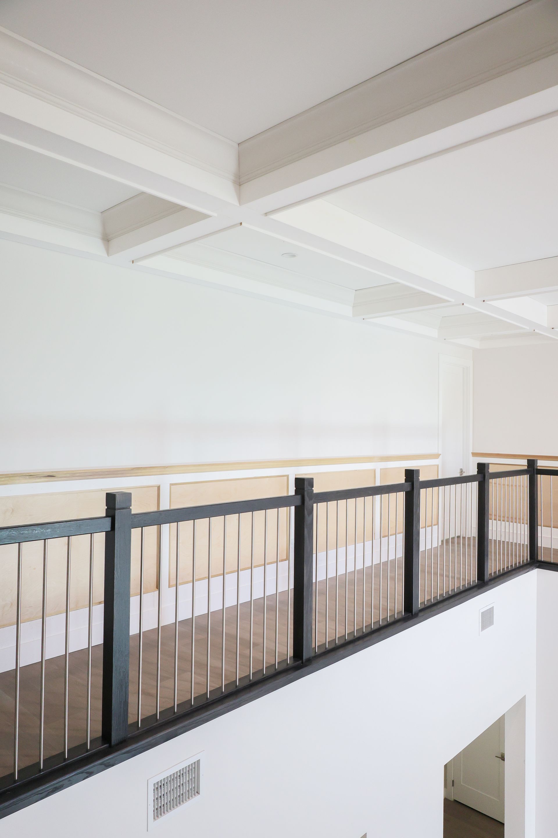 Bright interior balcony with black railing, white walls, and exposed ceiling beams