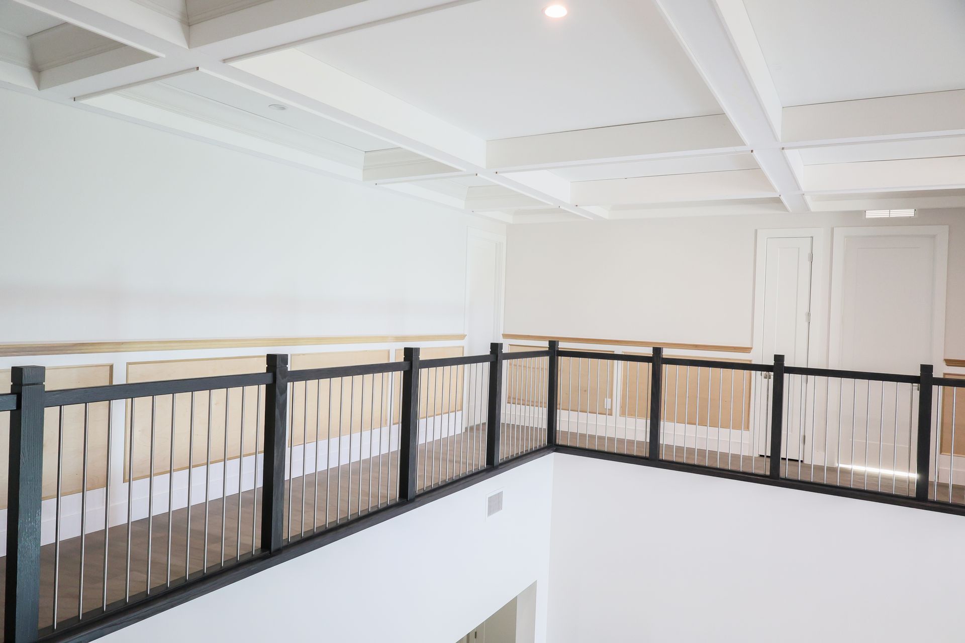 Bright upstairs landing with white walls, exposed ceiling beams, and black metal railing overlooking below