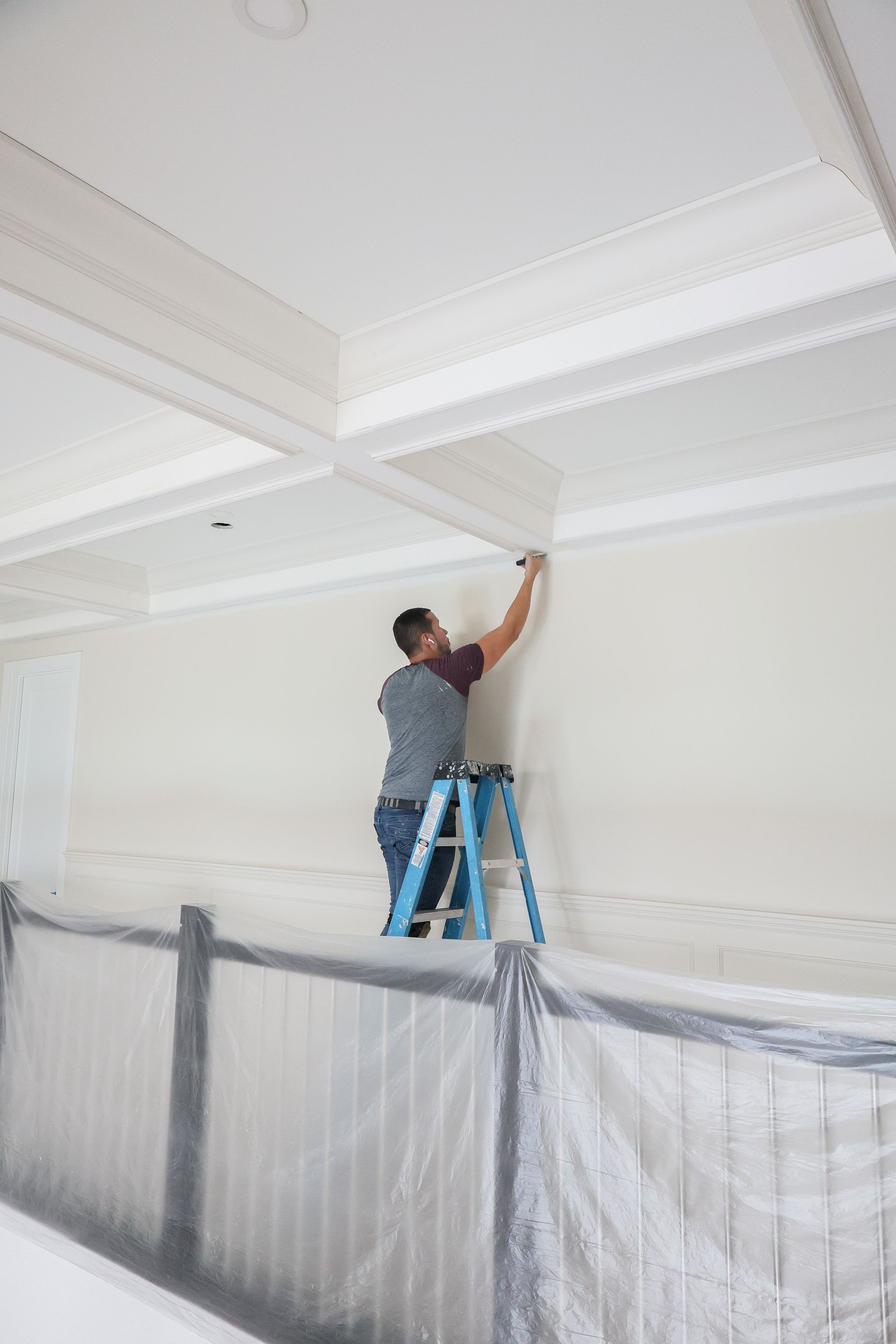 Person on a blue ladder painting or repairing a white ceiling in a room under renovation