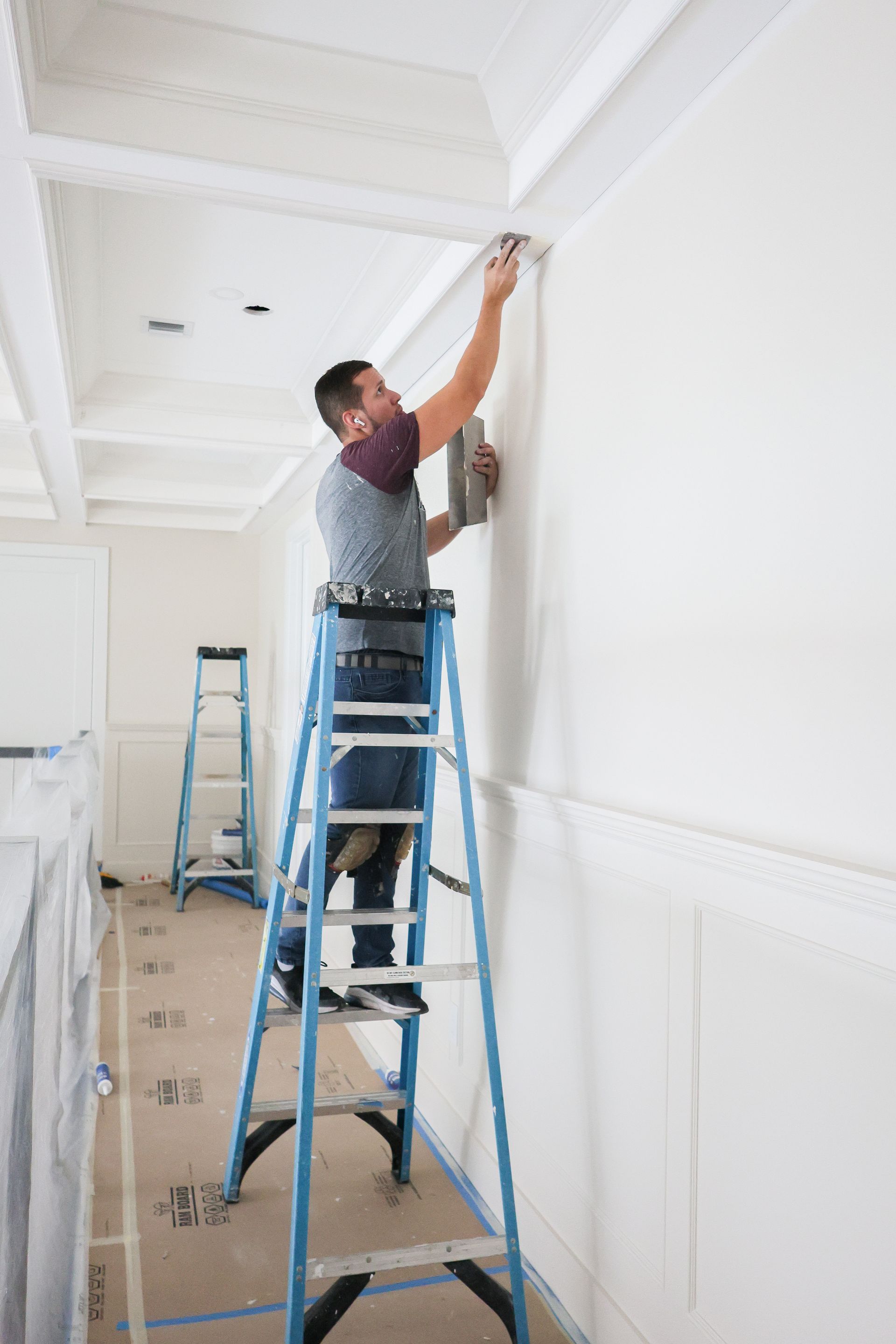 Person on a blue ladder painting a white wall in a bright room