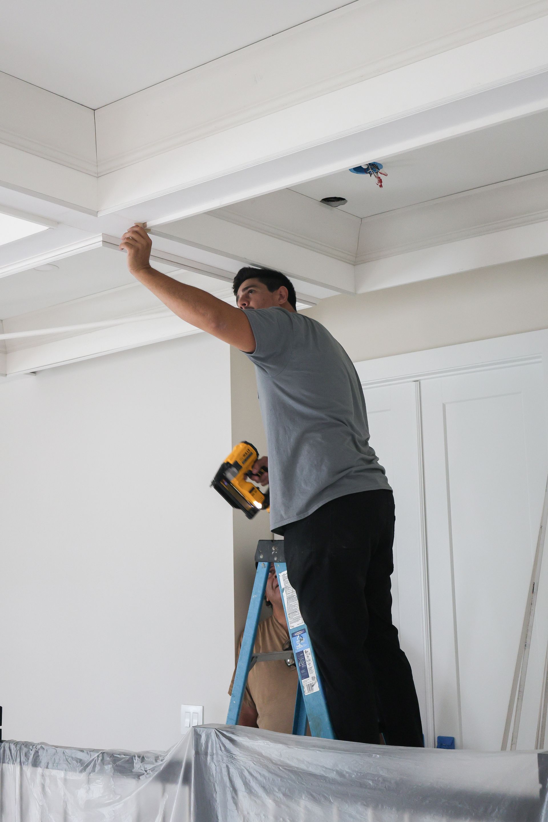 Man on a ladder painting a white ceiling in a room under renovation