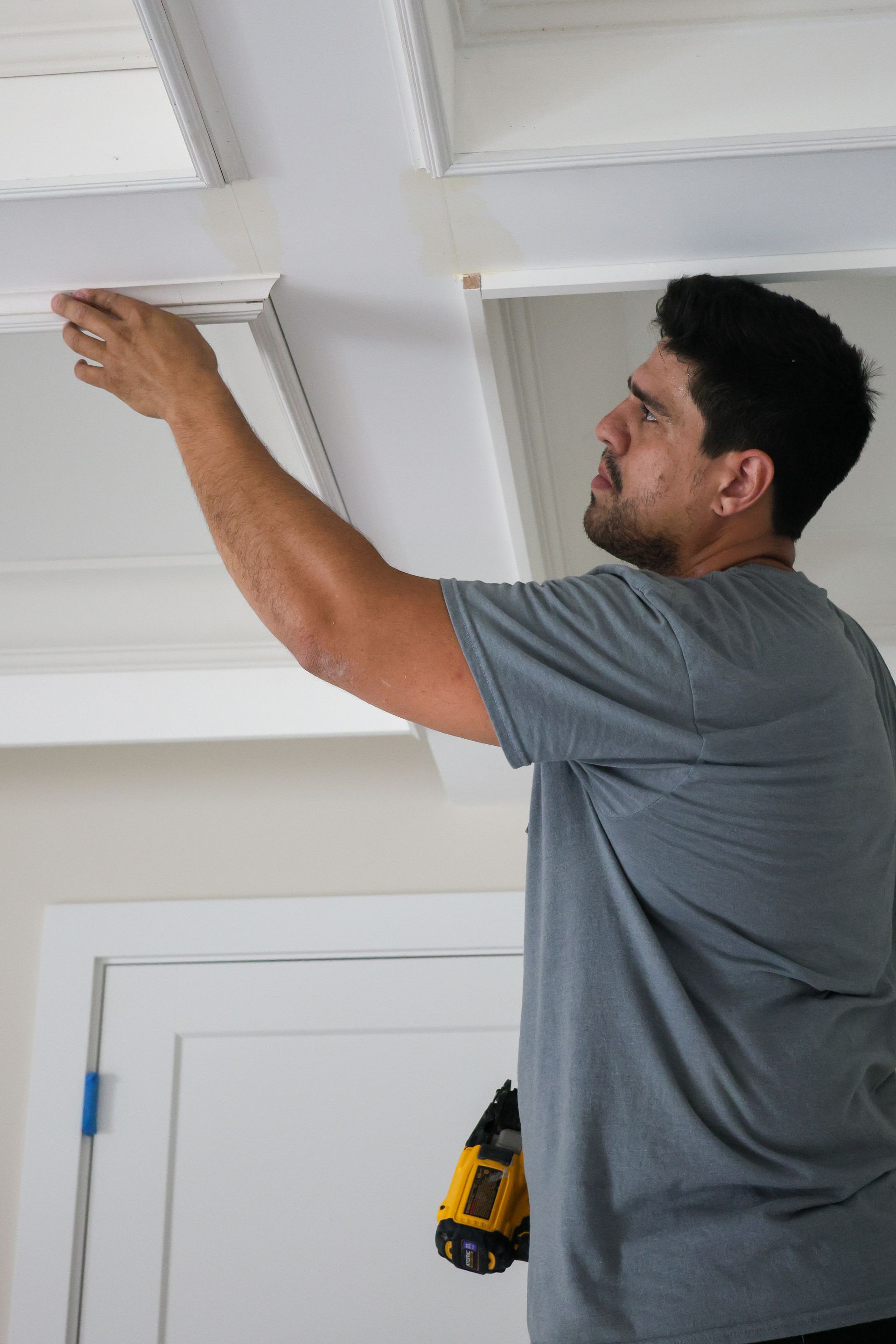 Man installing white ceiling molding with a cordless drill in a room