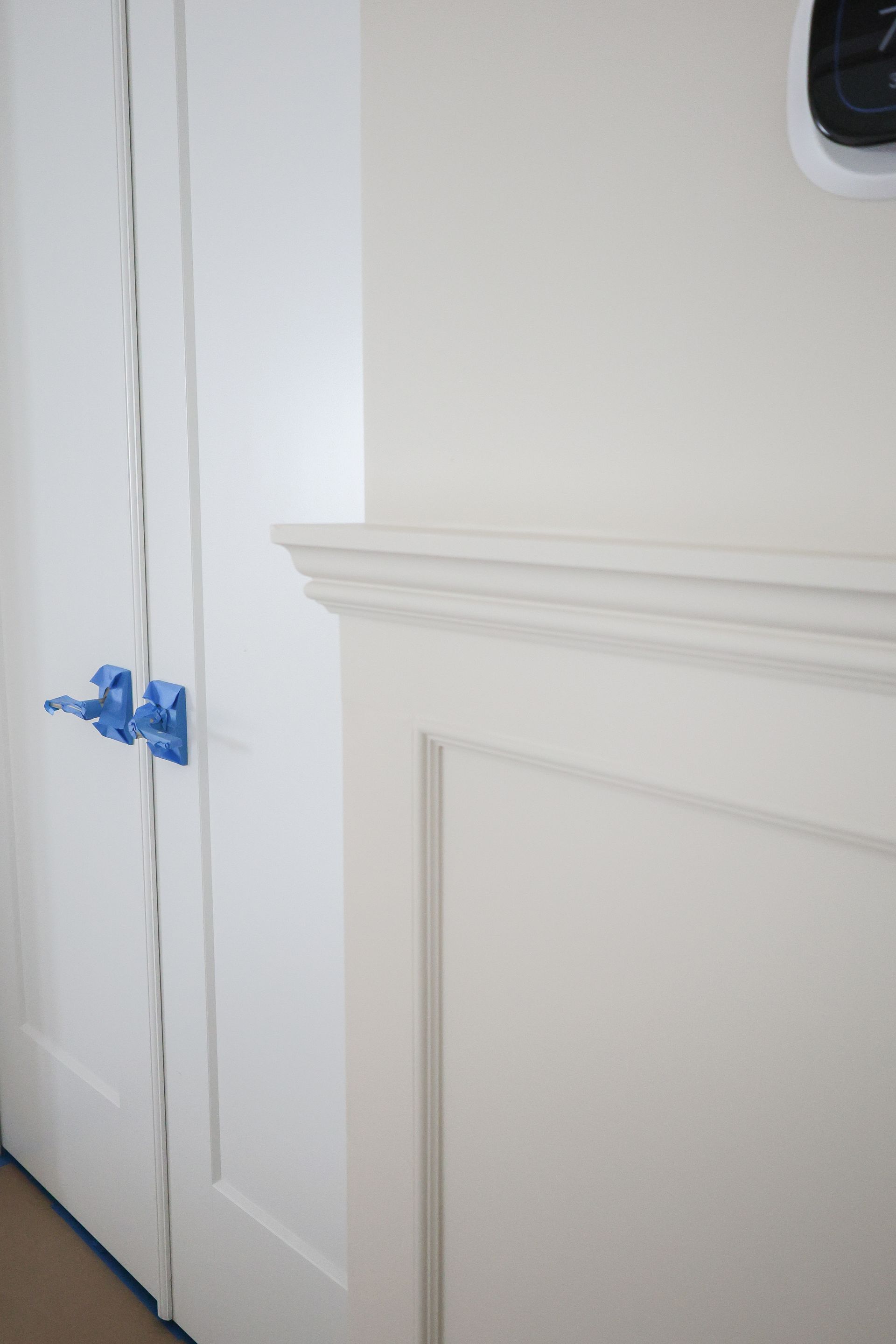 White paneled wall with blue painter’s tape and molding trim near a doorway