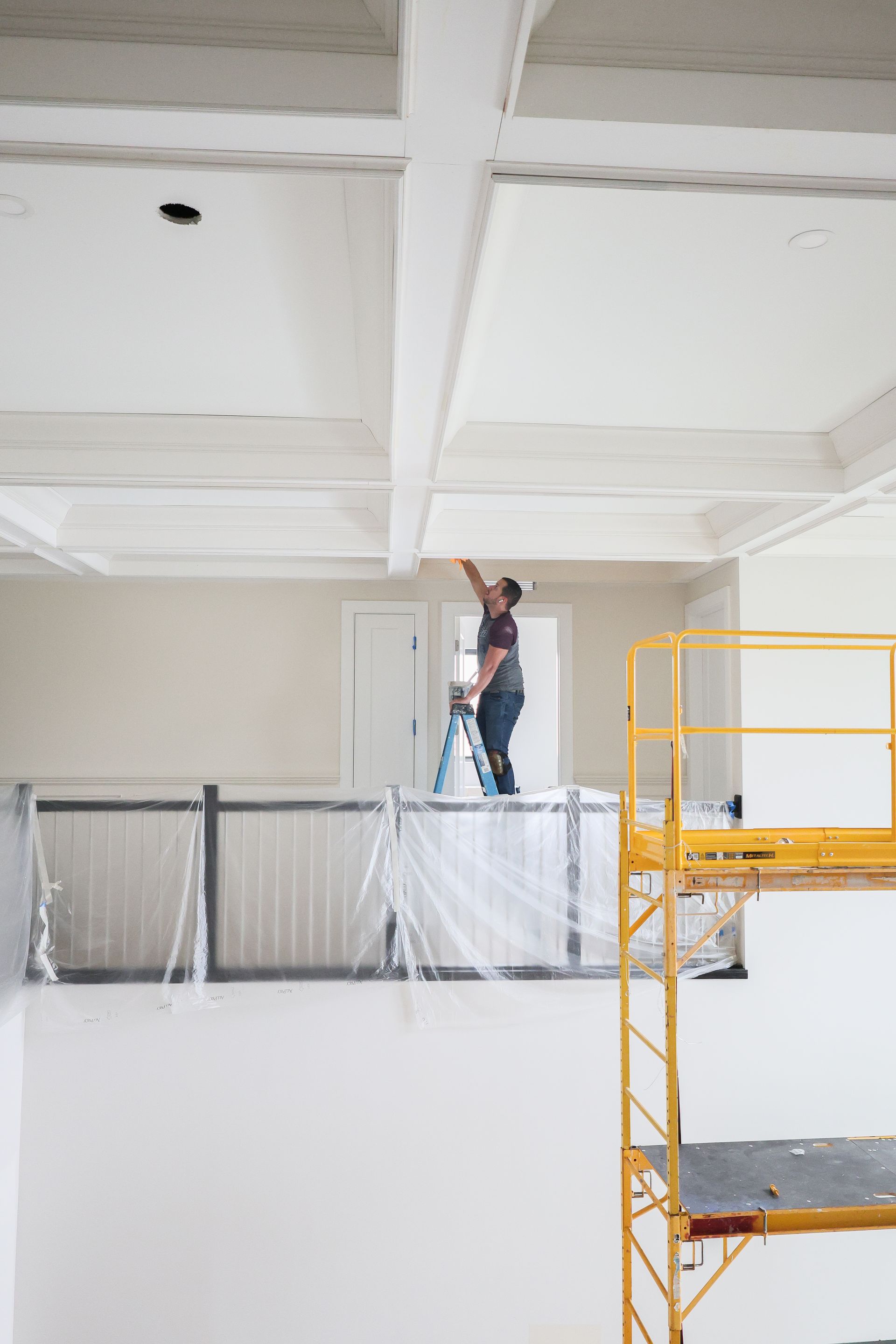 Worker painting a white ceiling near a yellow scaffold in a large industrial interior