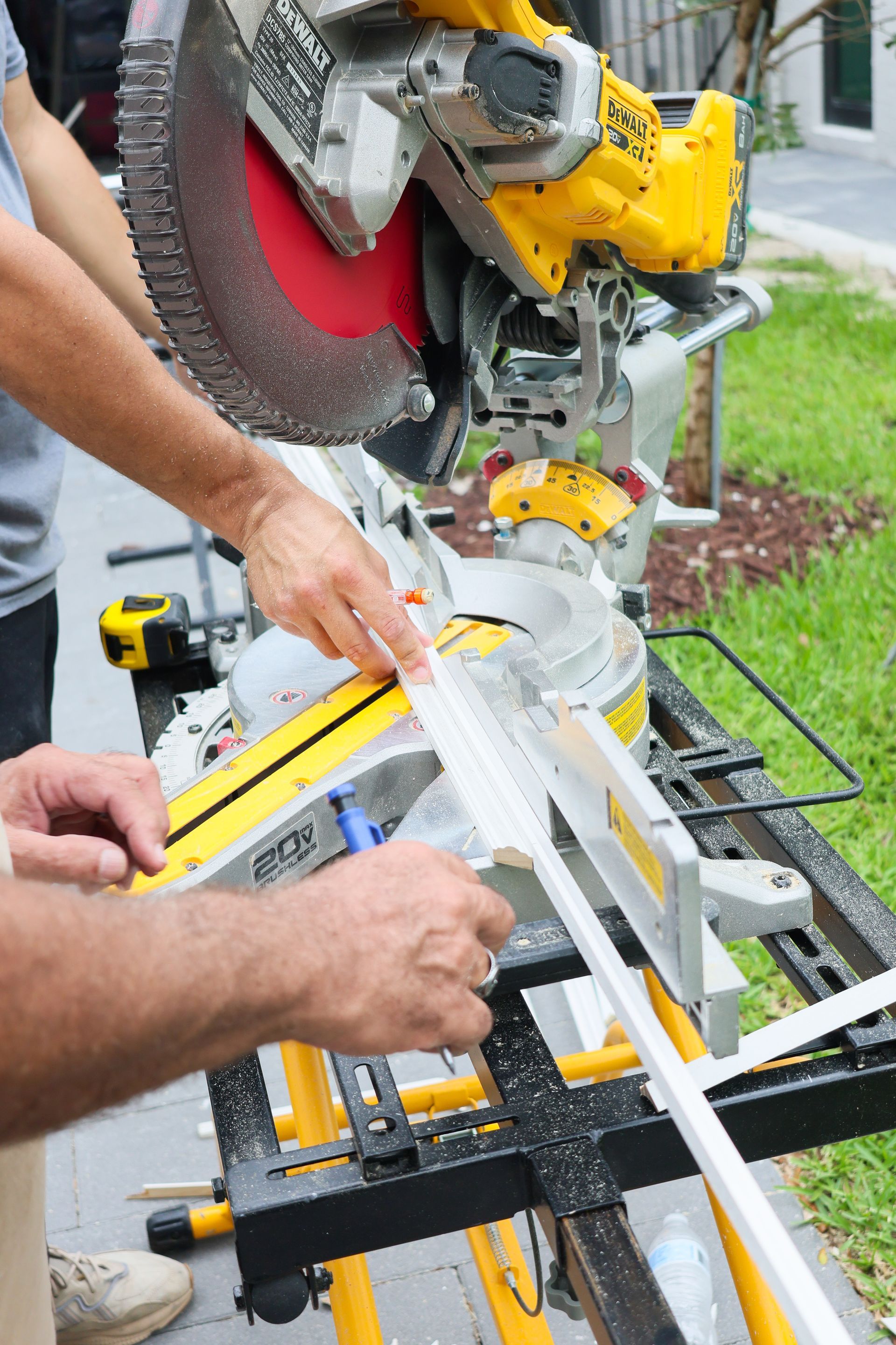 Person using a miter saw to cut a white board on a workbench outdoors