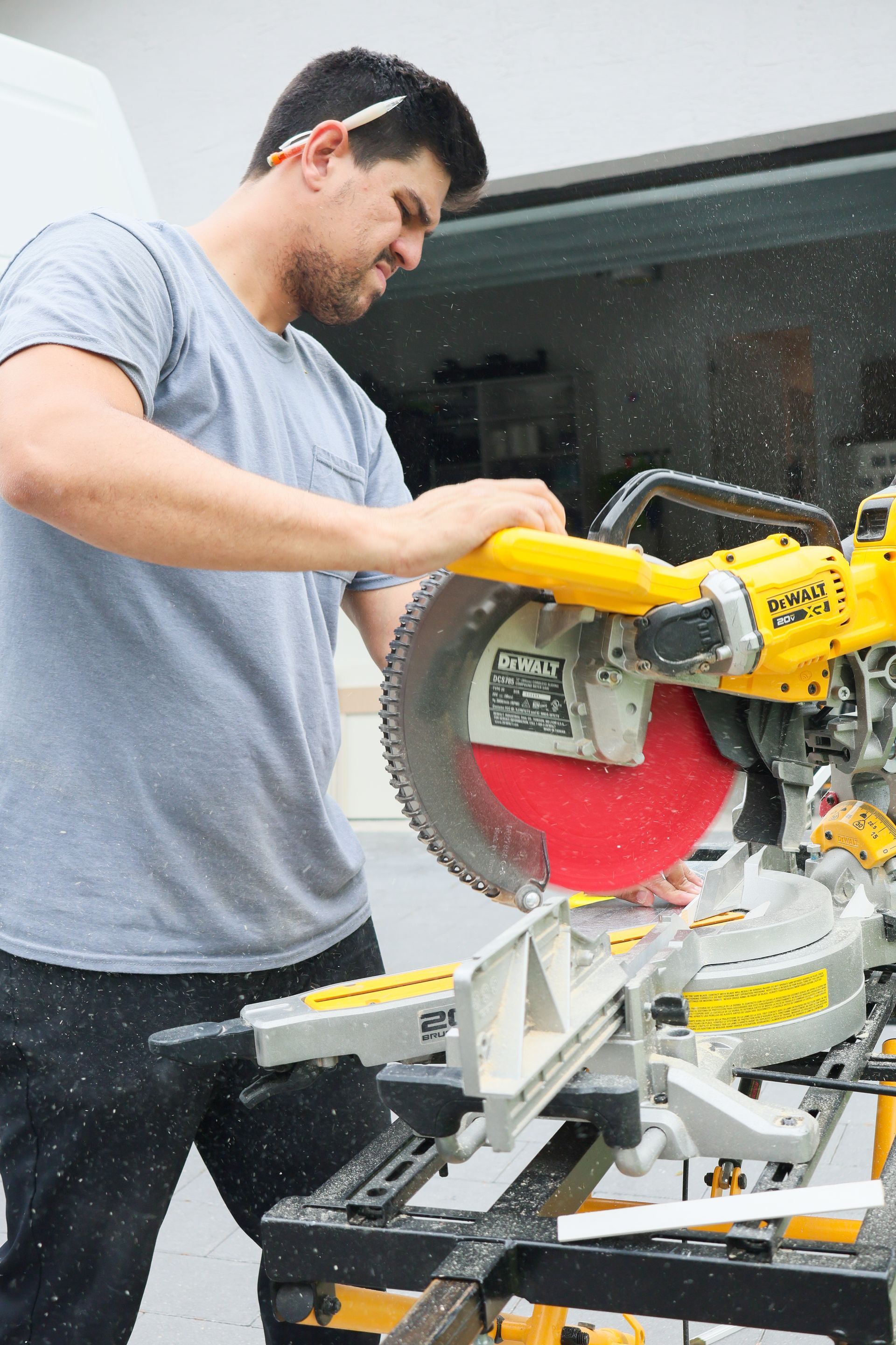 Worker operating a yellow miter saw in a workshop, cutting material with sawdust flying.