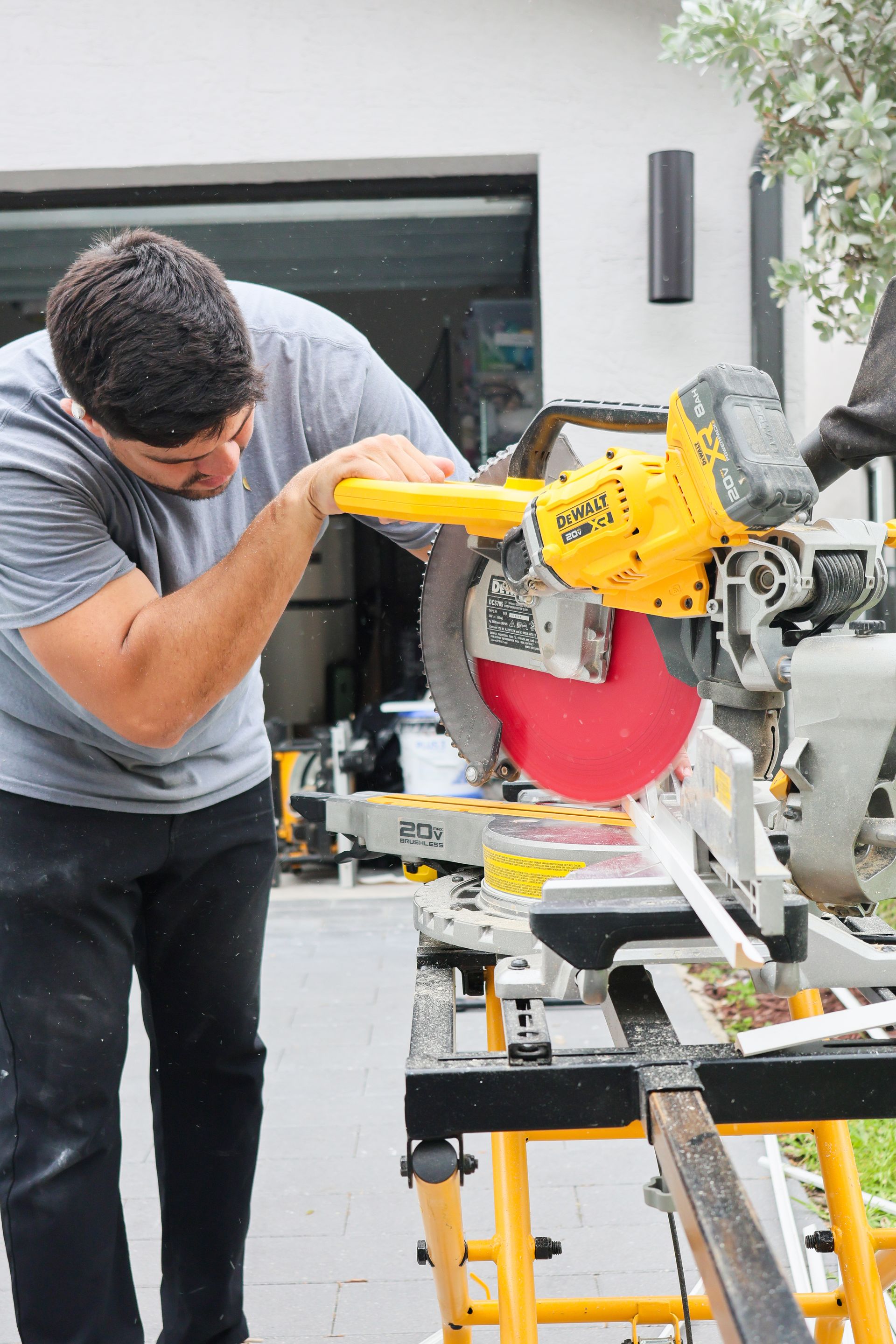 Person using a yellow miter saw to cut wood on a workbench in a garage/workshop.