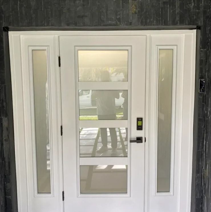 White front door with glass panels and sidelights on a dark exterior wall