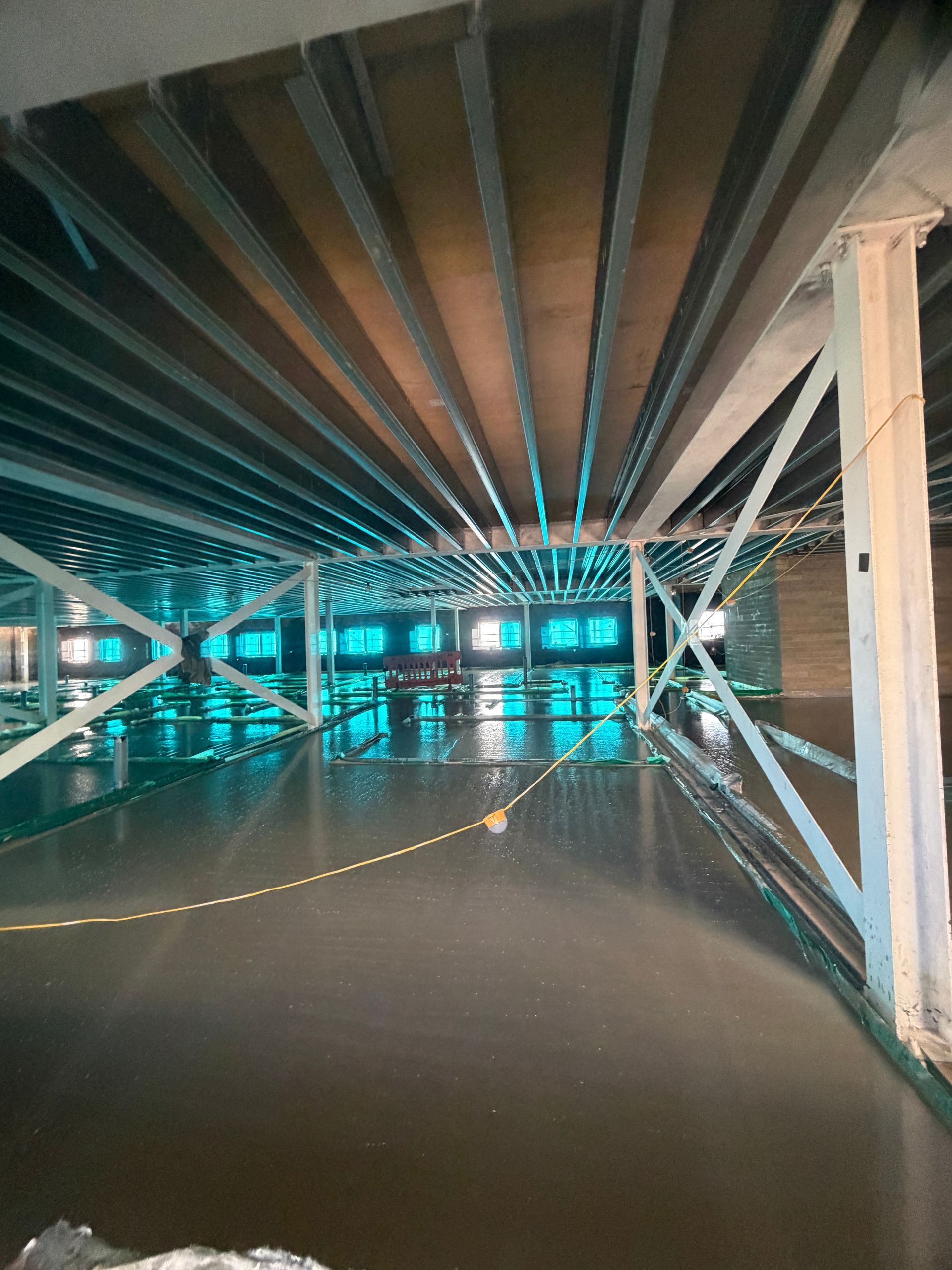 Low-ceiling waterfront underpass with dark water and green-blue lights reflecting on the surface