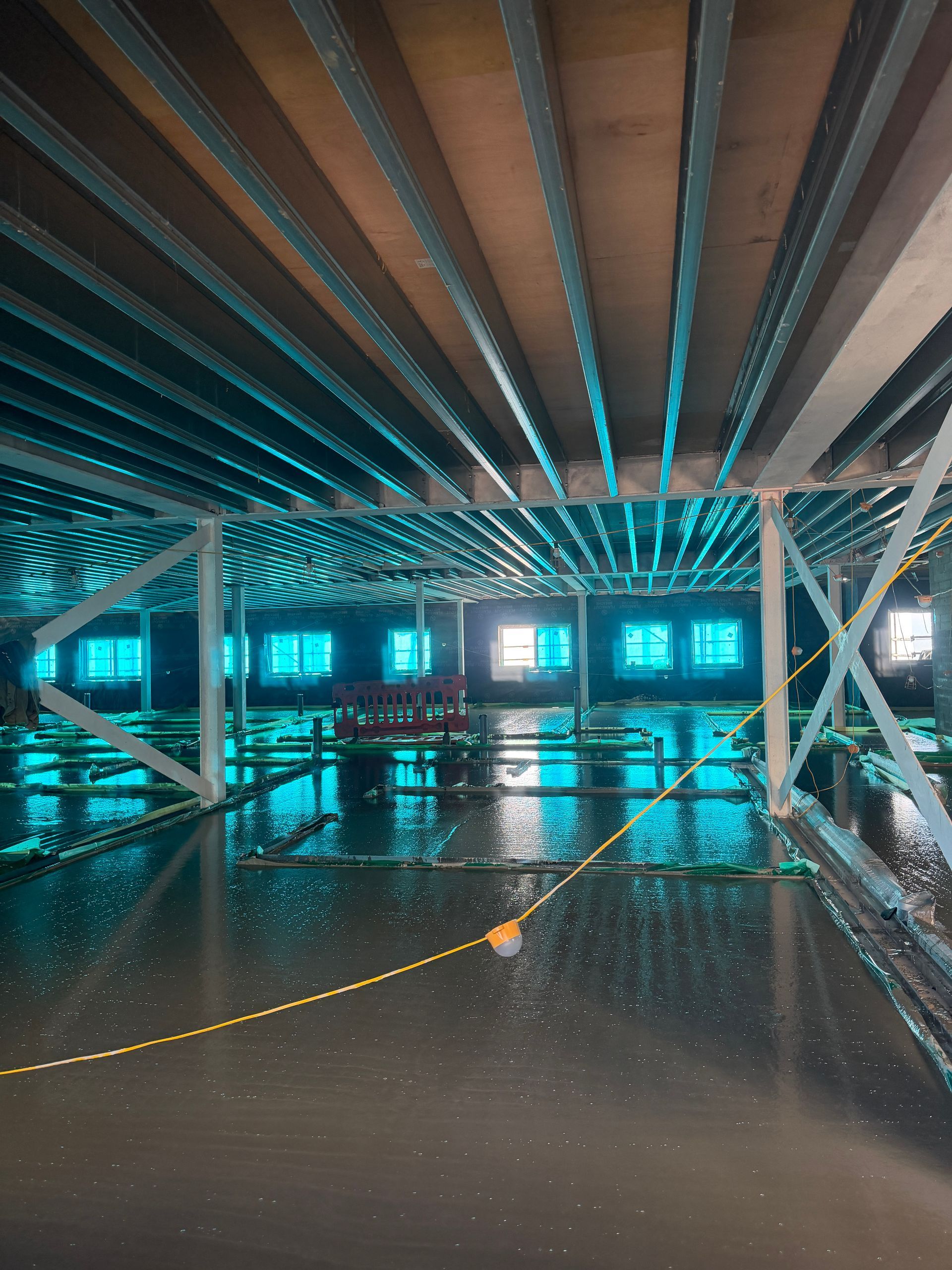 Empty industrial interior with wet floor, exposed beams, and cyan-lit windows.